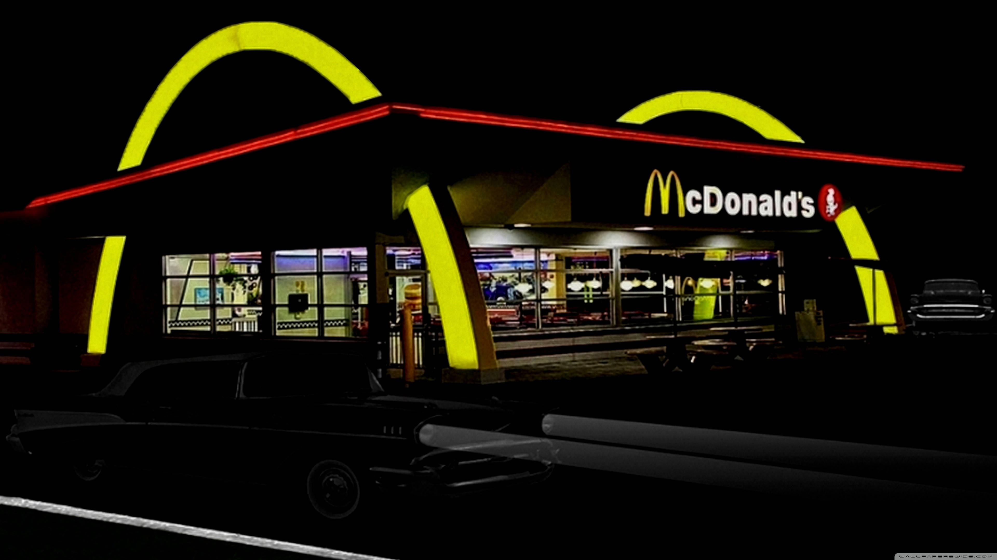 Mcdonalds 桌布 壁紙 — 夜晚發光的麥當勞餐廳，標誌性的金色拱門和紅色飾邊，前景是一輛經典汽車的剪影。