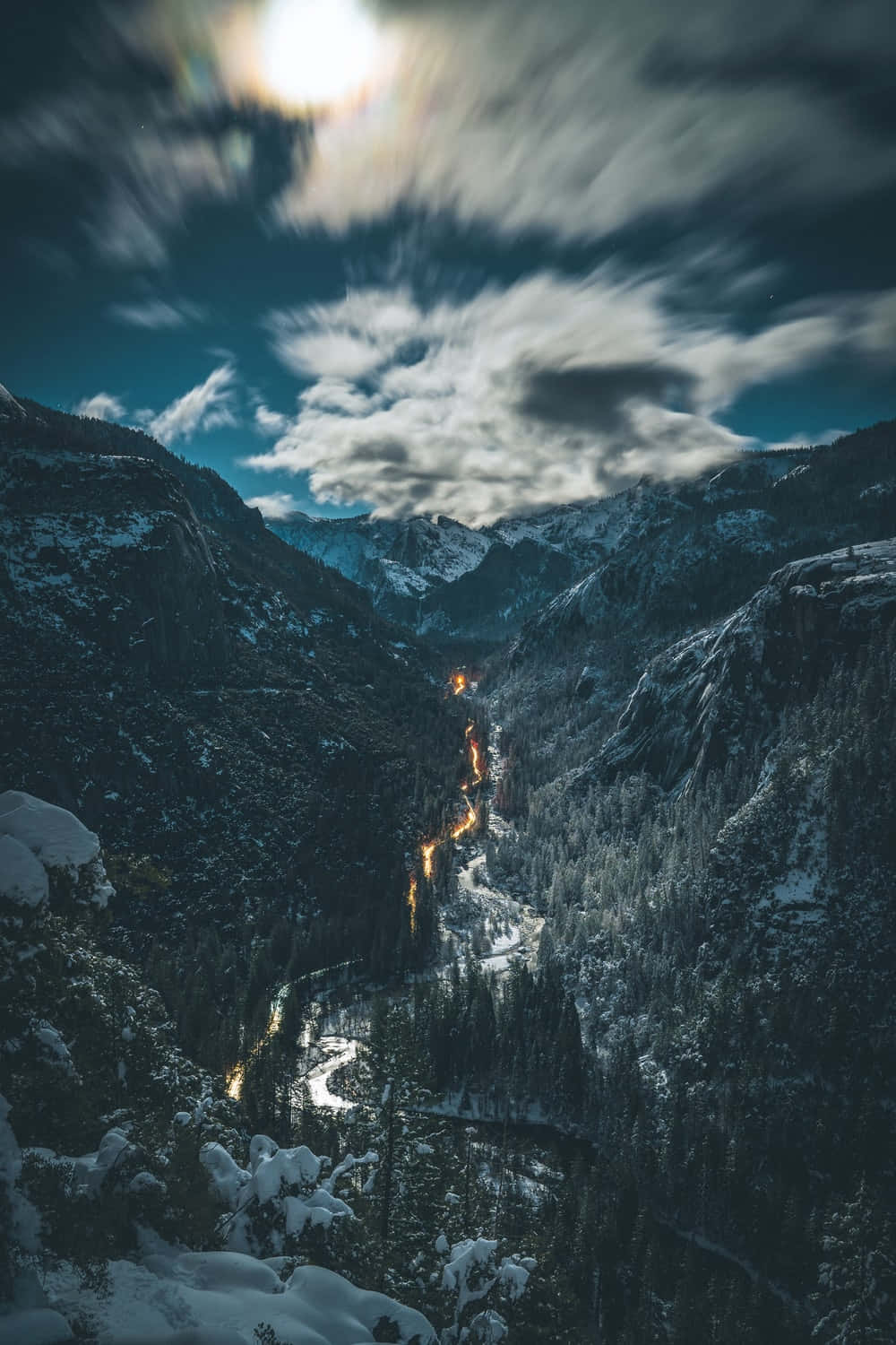 背景 桌布 壁紙 — 夜晚白雪覆蓋的山谷，有條紋雲和蜿蜒道路上的發光燈光。
