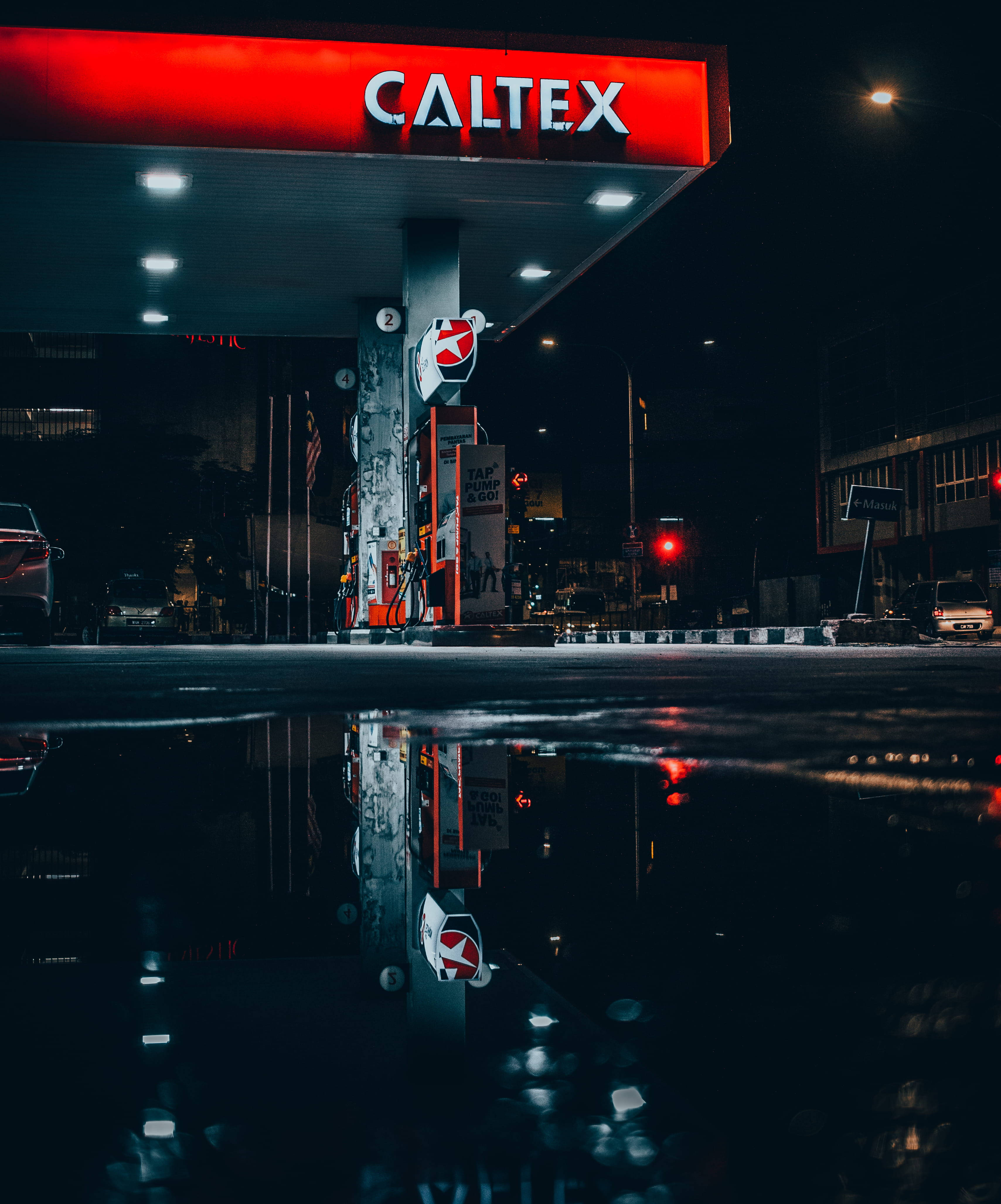 Gas Station 桌布 壁紙 — 夜晚的Caltex加油站，紅色標誌和油泵倒映在濕漉漉路面上的雨水坑中。