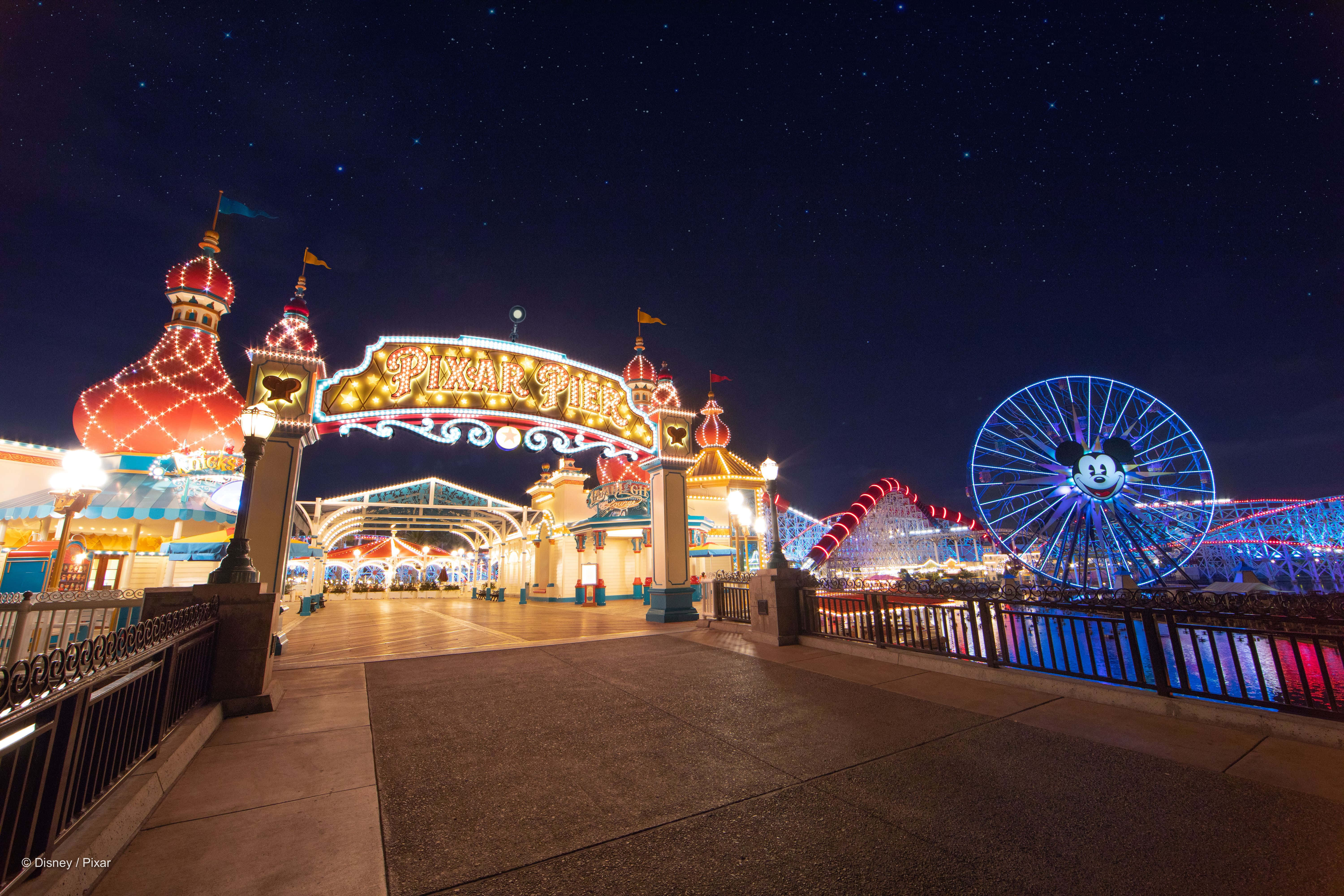 Disneyland 桌布 壁紙 — 夜晚的Pixar Pier在星空下閃耀，色彩繽紛的摩天輪和節日燈光照亮入口。