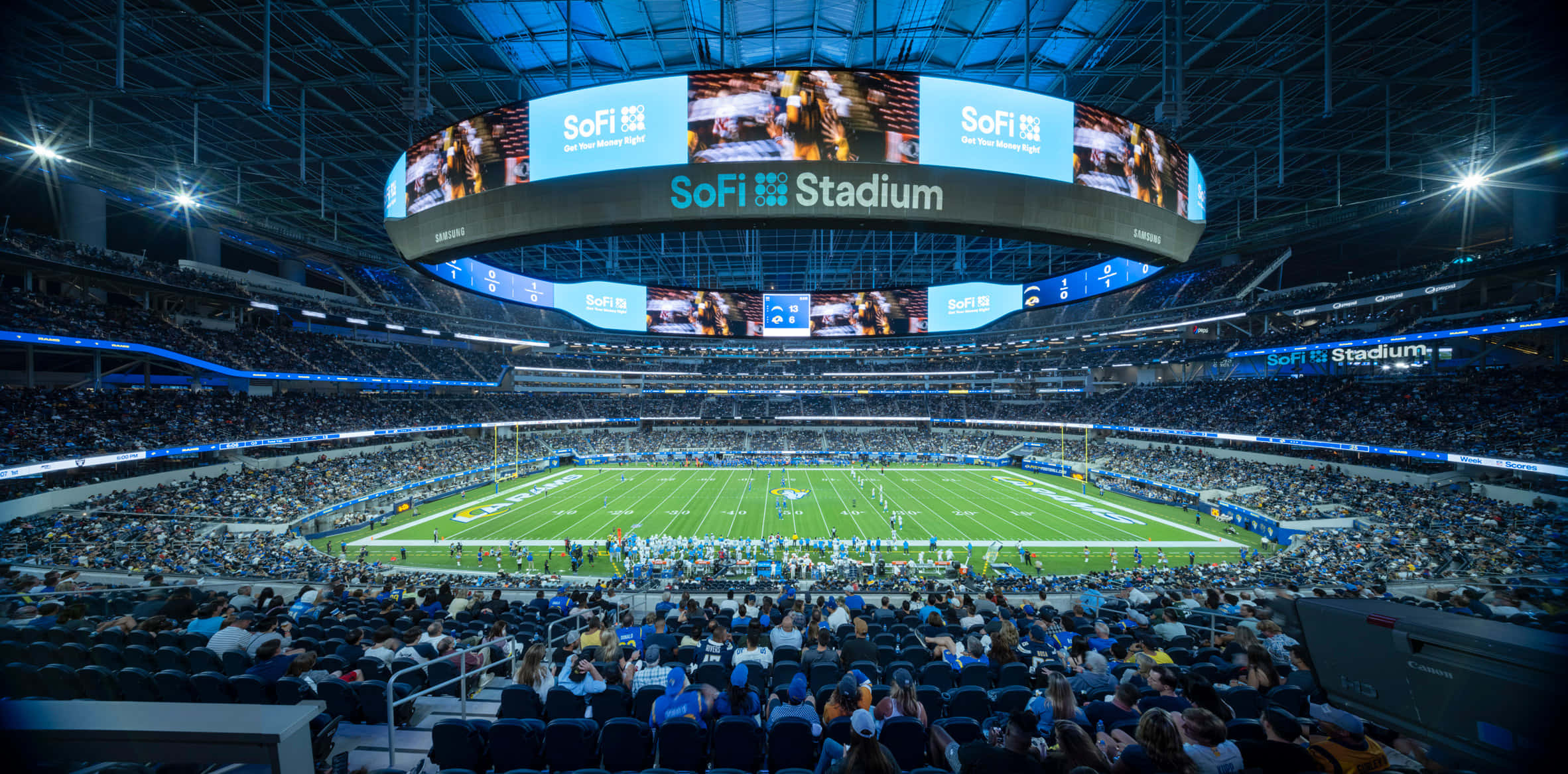 Sofi Stadium 桌布 壁紙 — 夜晚的SoFi體育館寬闊鏡頭，充滿了在明亮燈光下觀看足球比賽的粉絲。