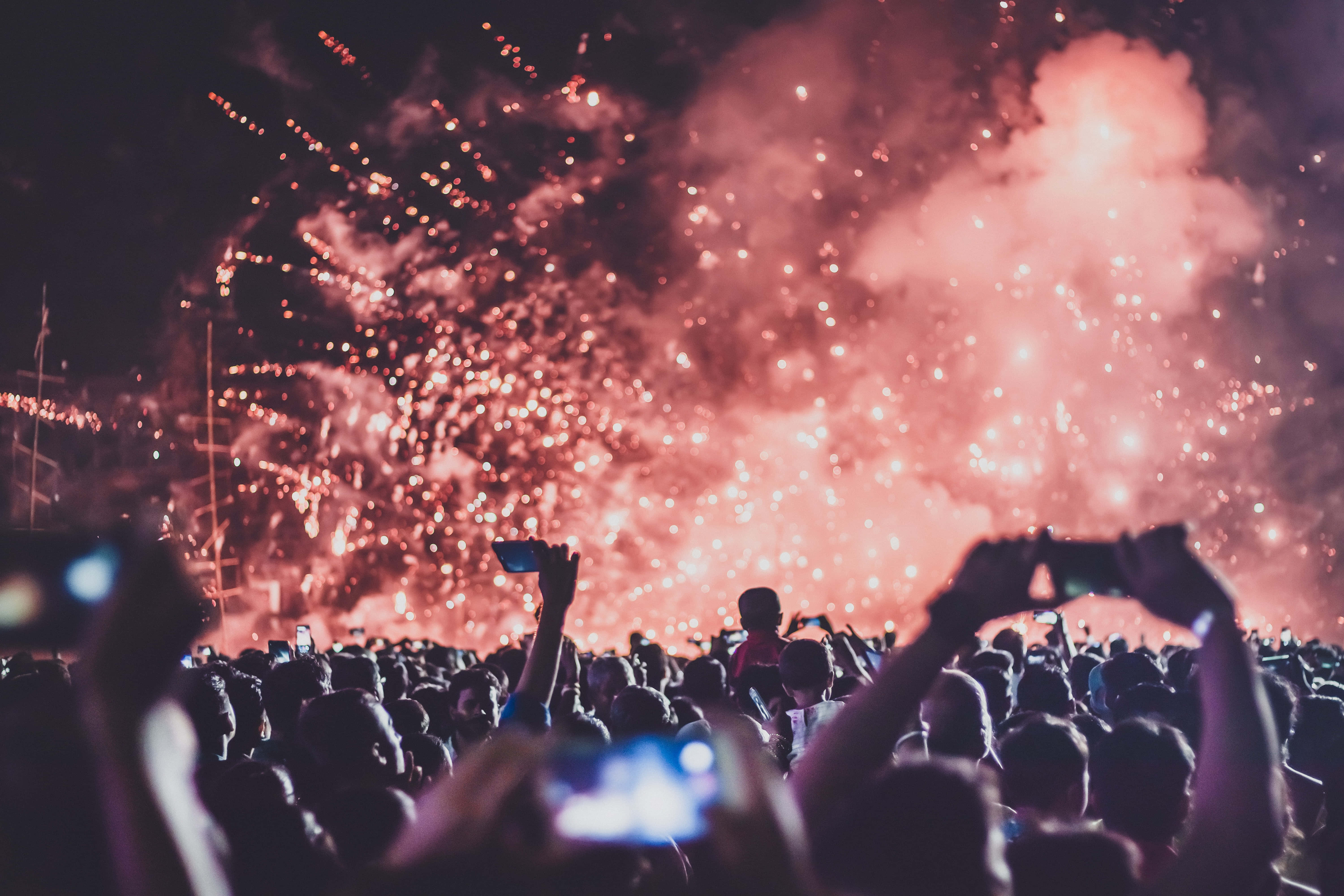 music festival 桌布 壁紙 — 夜晚的人群舉起手機捕捉頭頂上綻放的耀眼紅色煙火。