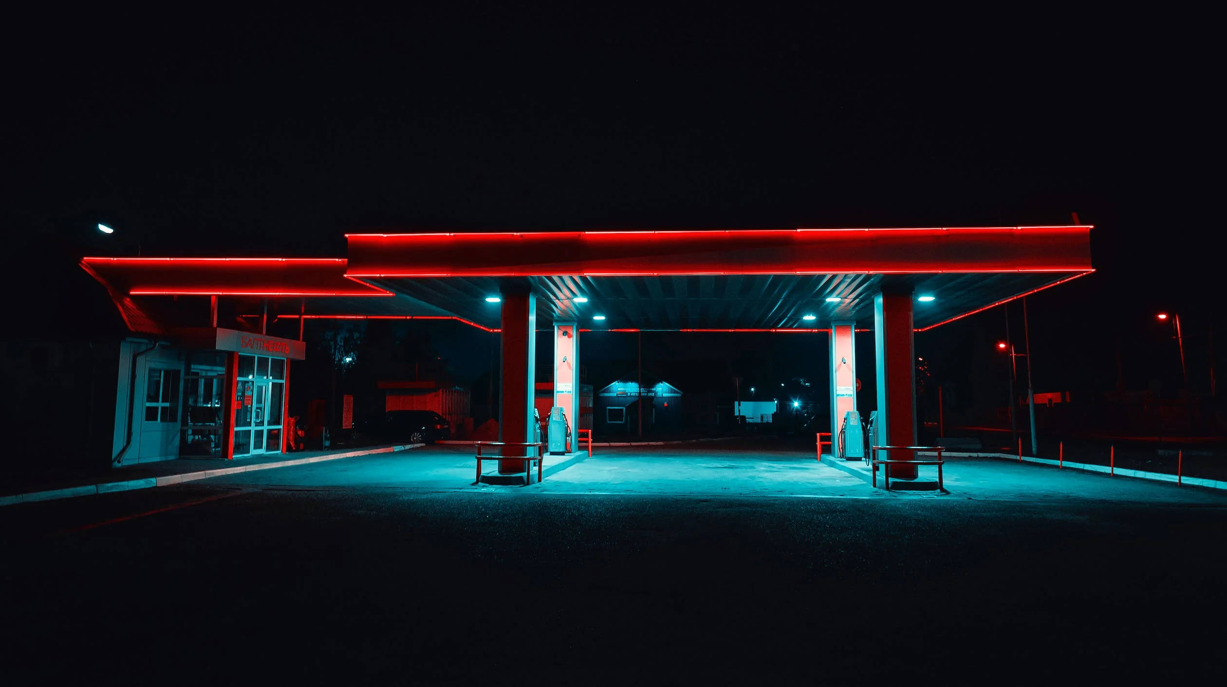 夜晚 桌布 壁紙 — 夜晚的加油站，被醒目的紅色和青色霓虹燈照亮，在空蕩蕩的路面上投下戲劇性的陰影。