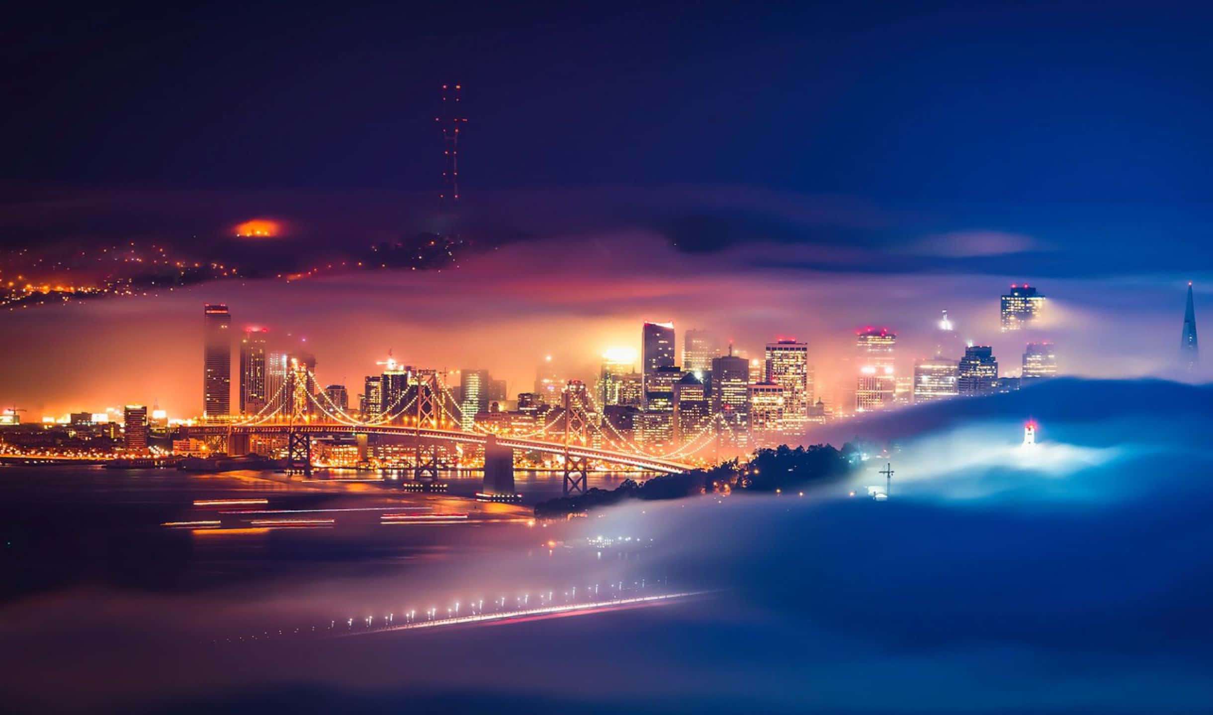 2440x1440 San Francisco 桌布 壁紙 — 夜晚的城市天際線，發光的燈光穿過霧氣籠罩的雲層，照在橋樑和水面上。