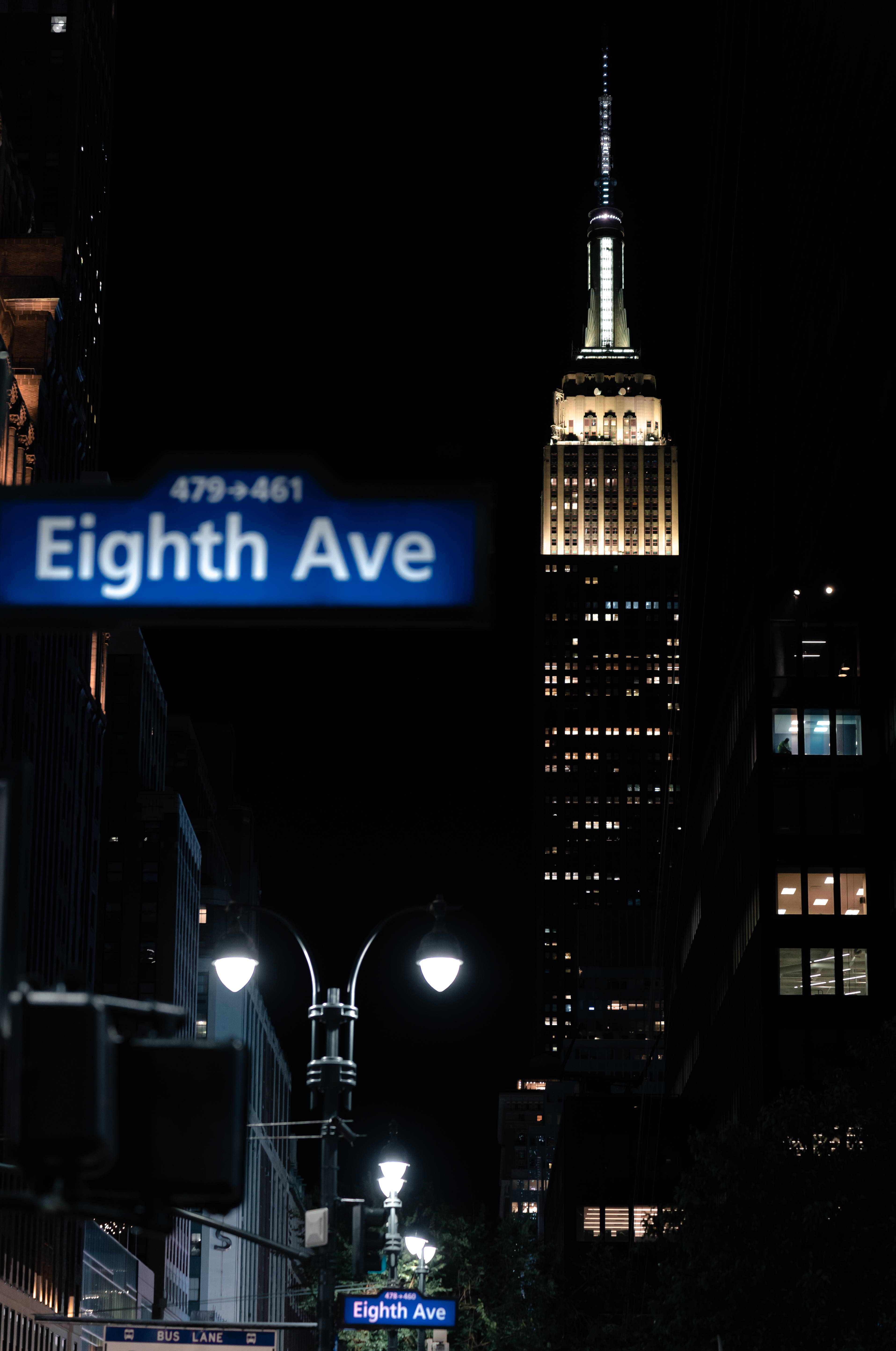 empire state 桌布 壁紙 — 夜晚的城市景觀，亮燈的帝國大廈聳立在第八大道的路牌上方，伴隨著發光的街燈。