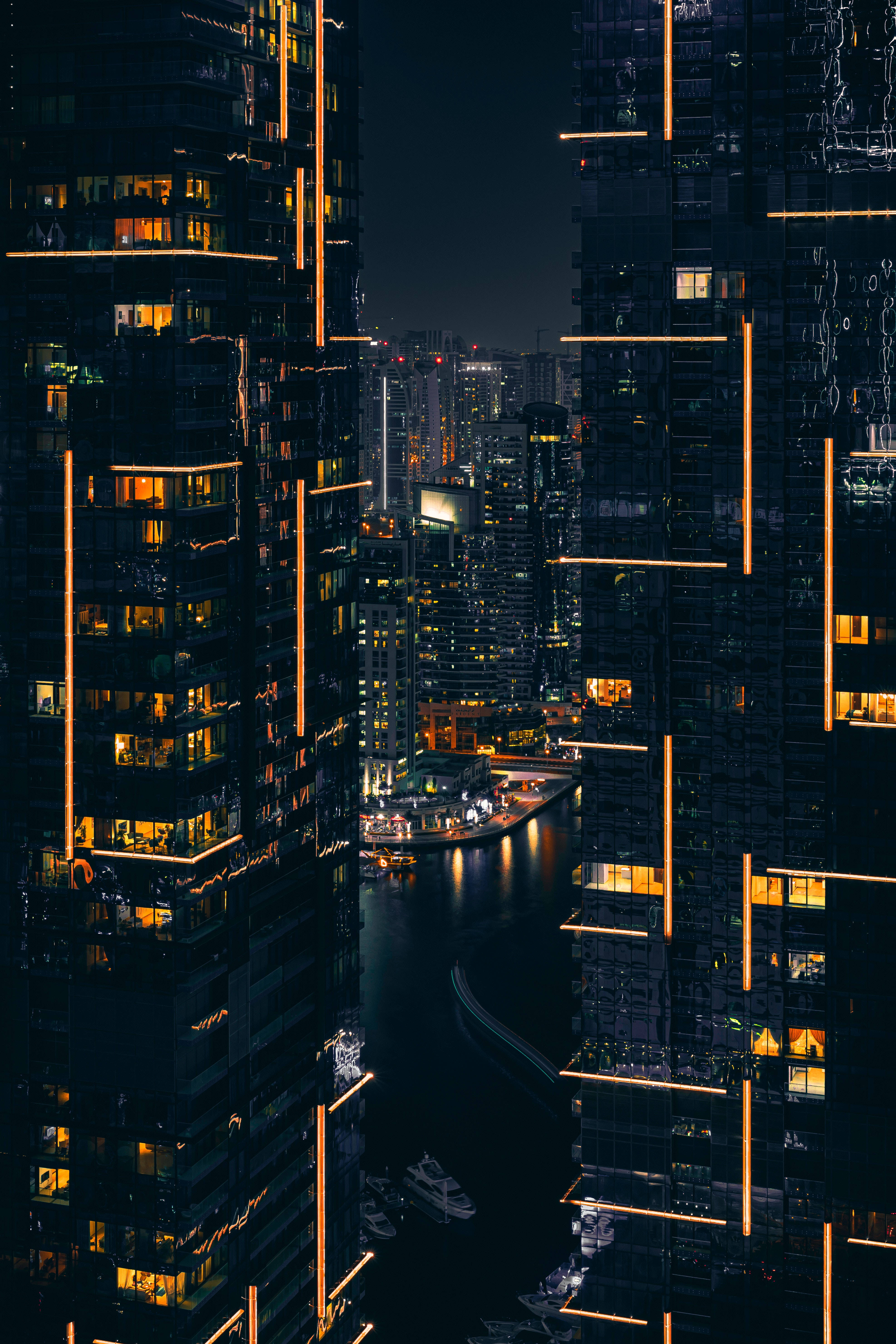 Light 桌布 壁紙 — 夜晚的城市景觀，由高聳的摩天大樓框住，琥珀色的燈光在下方黑暗的水道上反射。