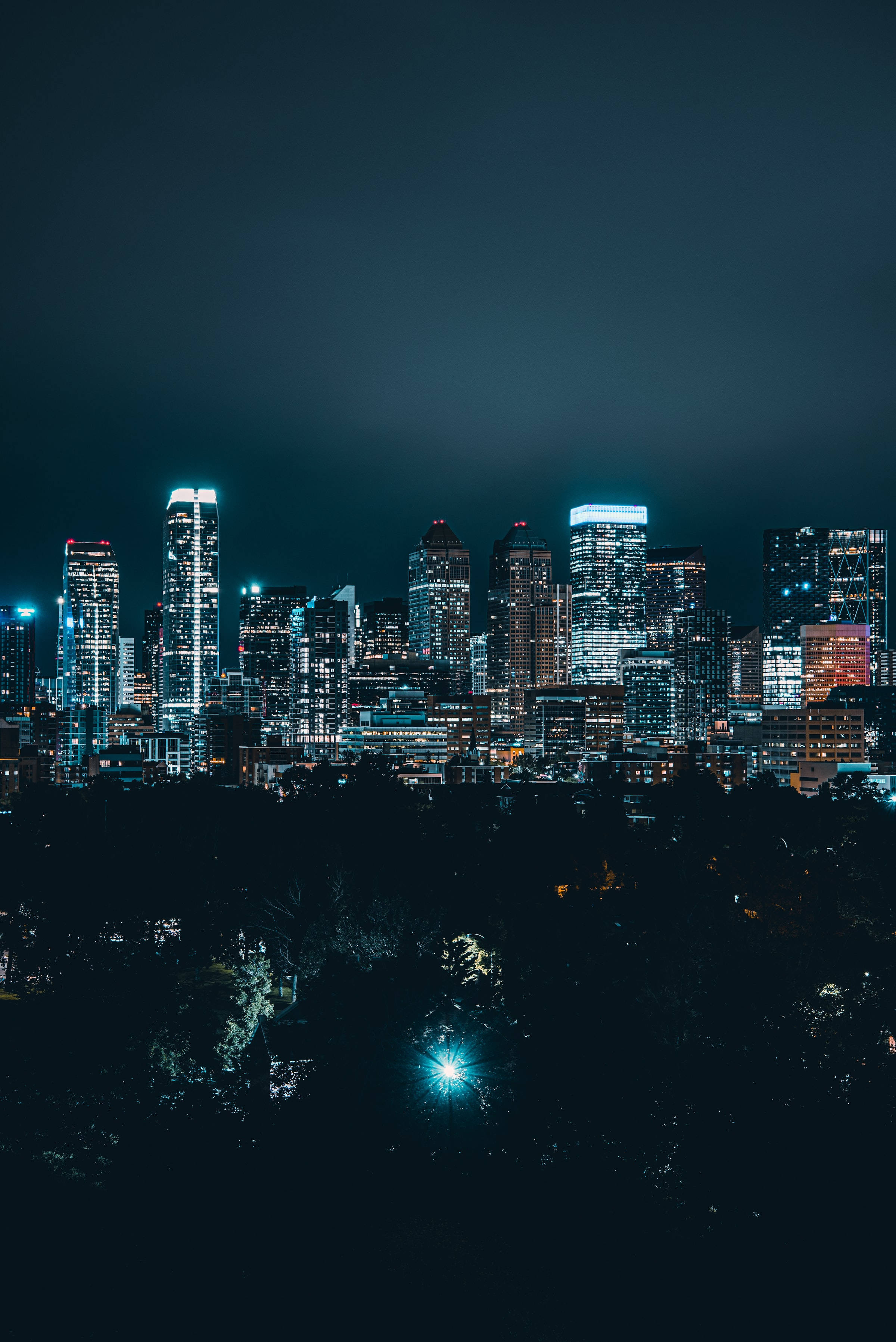 Night Aesthetic 桌布 壁紙 — 夜晚的城市景觀，高聳的摩天大樓在黑暗的天空中閃爍著藍色和白色的燈光。