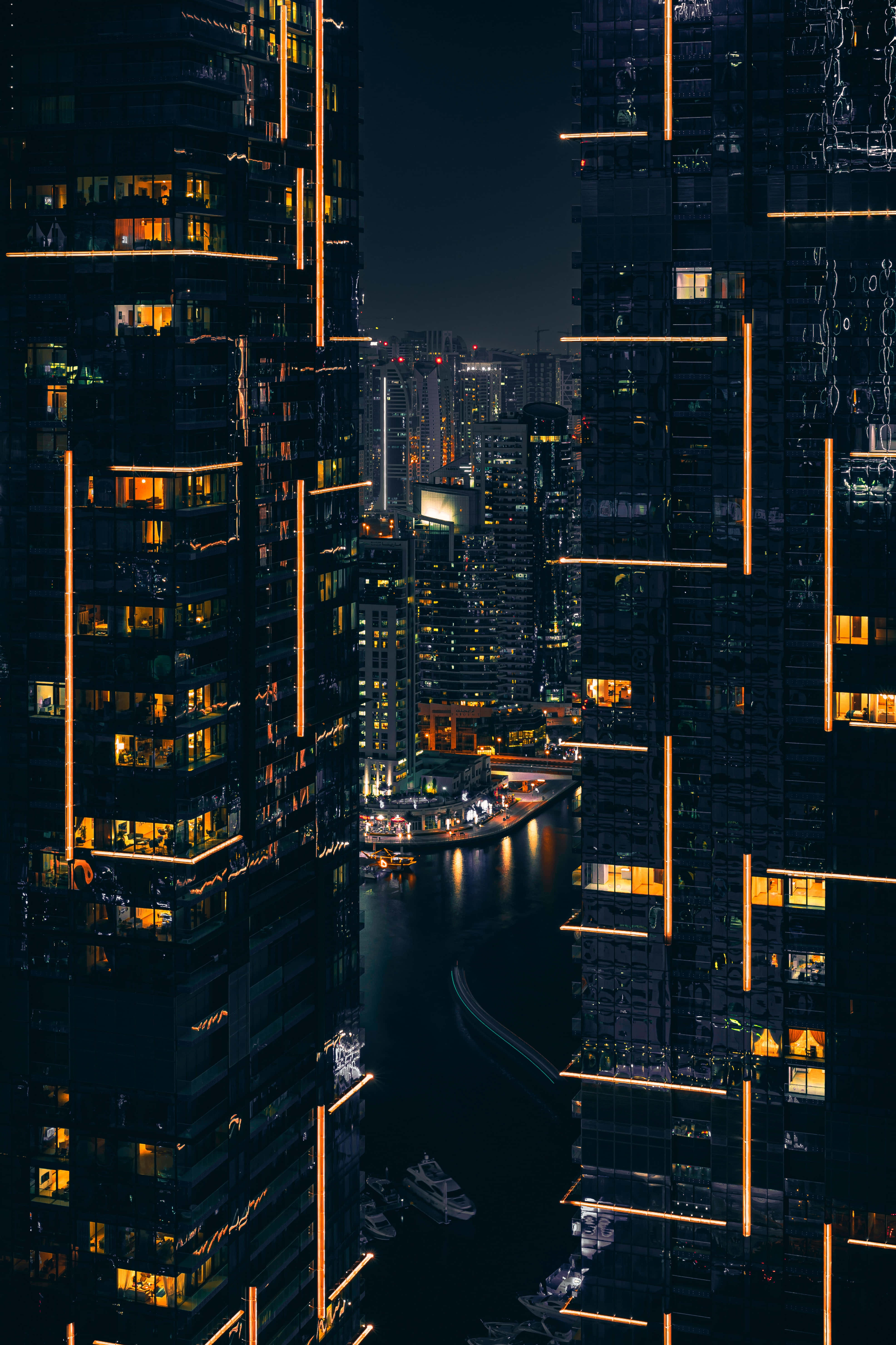 夜景城市 桌布 壁紙 — 夜晚的城市景觀，高聳的摩天大樓沿著黑暗的水道散發溫暖的光芒。