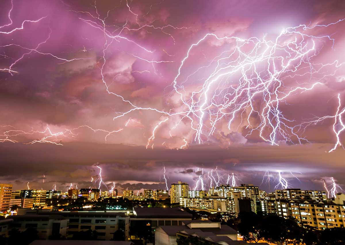 閃電 桌布 壁紙 — 夜晚的城市景觀被巨大的紫色雷暴照亮，鋸齒狀的閃電劃破天空。