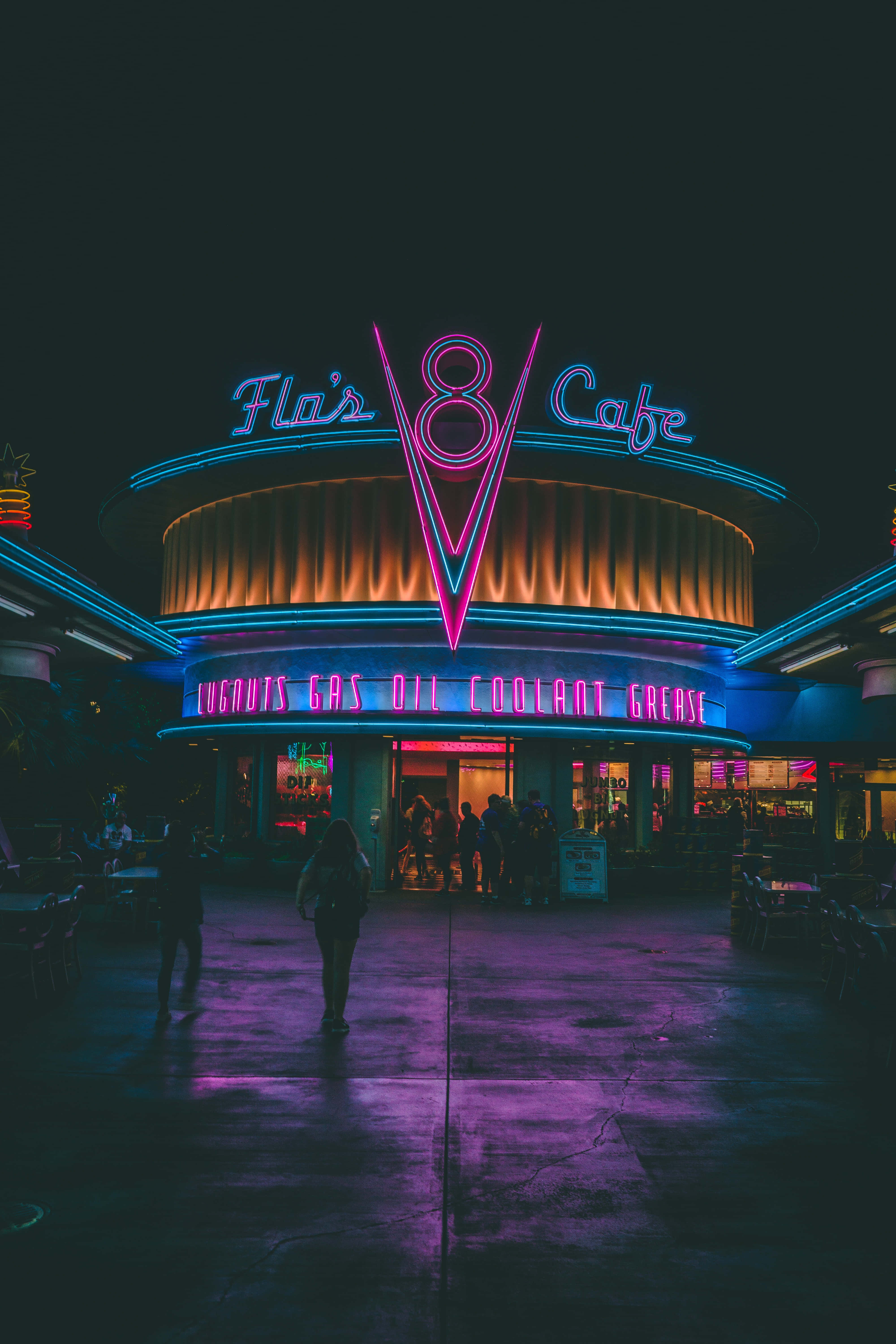 Neon City Aesthetic 桌布 壁紙 — 夜晚的復古餐廳閃爍著鮮豔的霓虹燈招牌，將紫色和藍色的光投射在潮濕的人行道上。