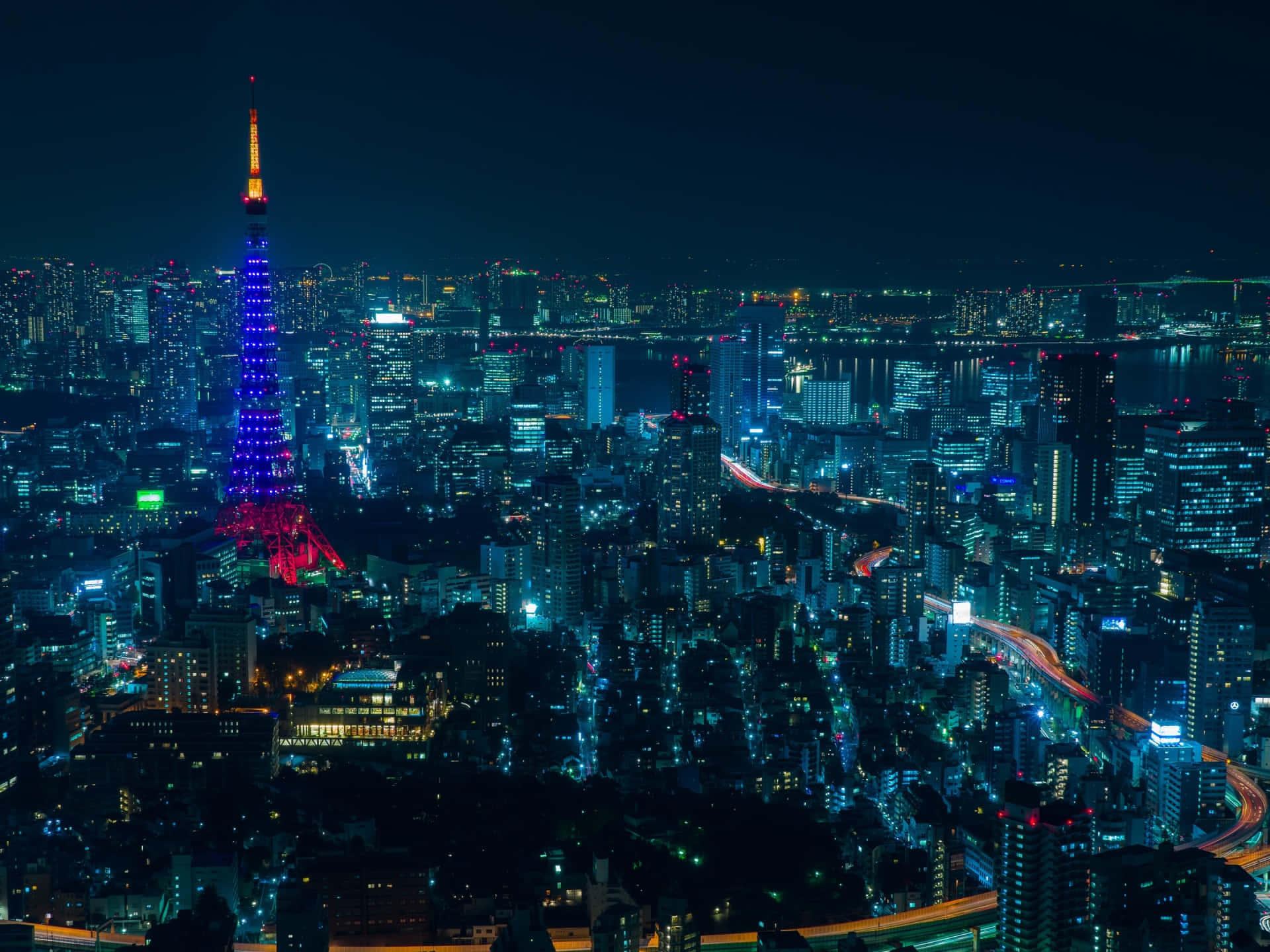 東京 桌布 壁紙 — 夜晚的東京天際線，東京塔在霓虹燈海和發光的道路中閃耀著紫色和紅色。