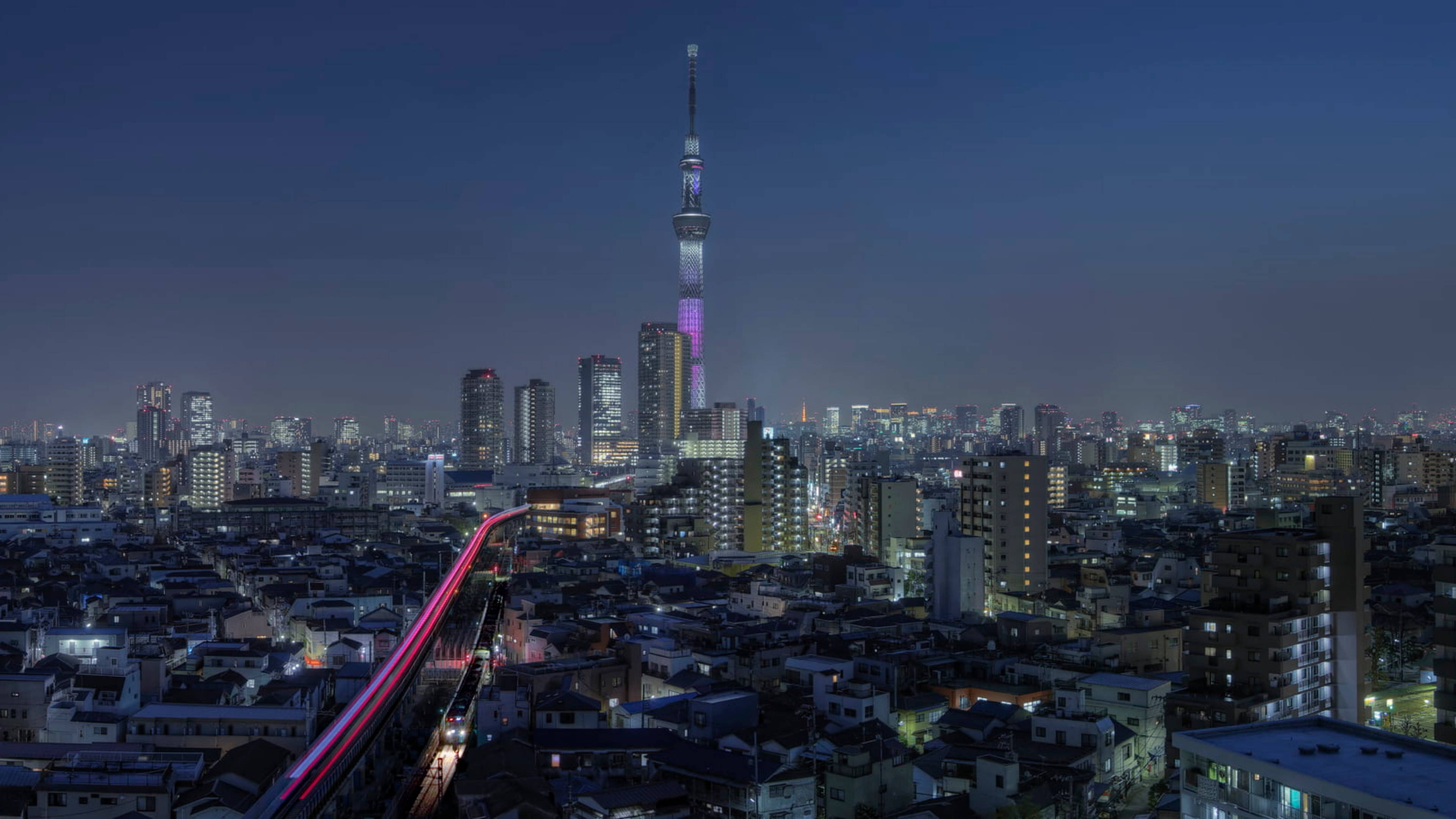 lights 桌布 壁紙 — 夜晚的東京天際線，東京晴空塔發出紫色和粉紅色的光芒，以及一列經過的火車留下的光跡。