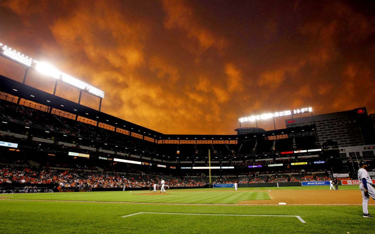 Baseball Stadium 桌布 壁紙 — 夜晚的棒球場，火橙色天空下，場上有球員，看台上有球迷。