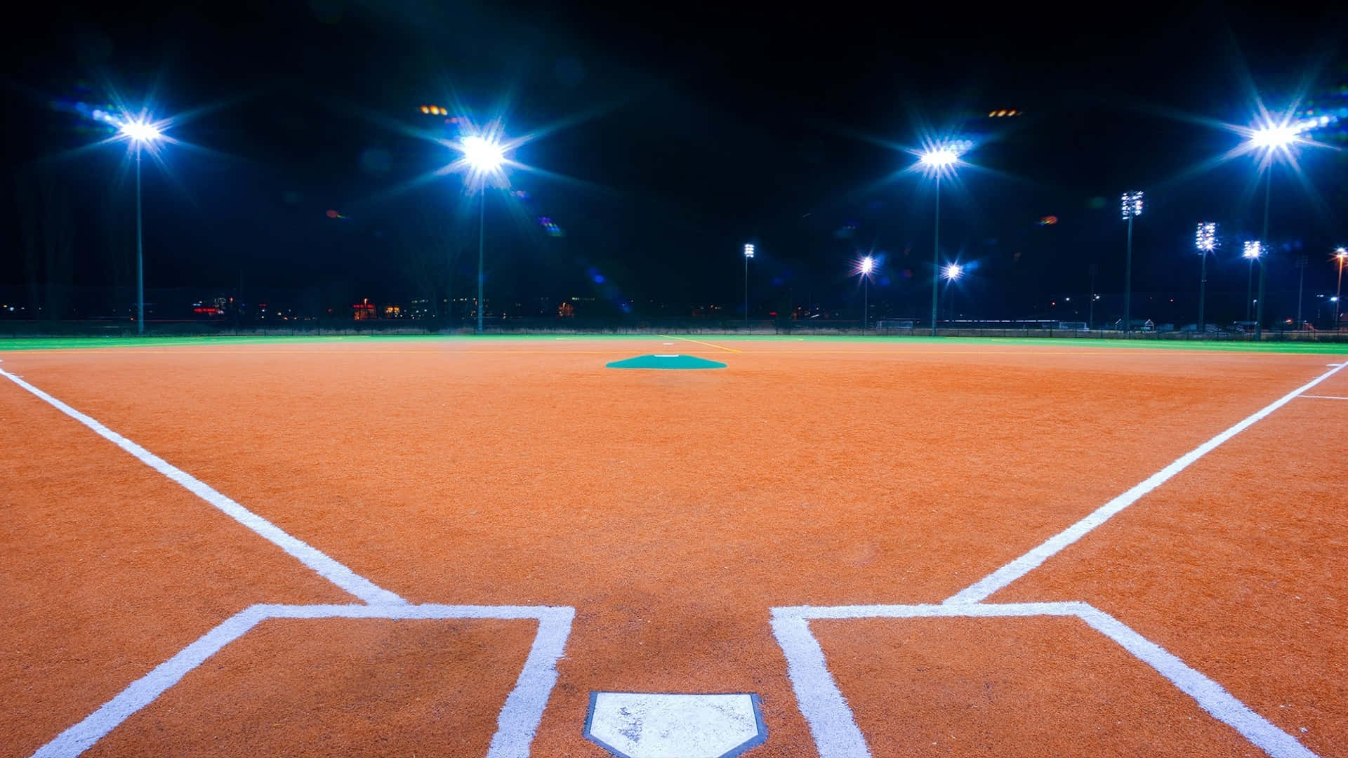 Baseball Field 桌布 壁紙 — 夜晚的棒球場明亮地照亮，體育場的燈光閃耀，照亮了橙色的泥土和白色的粉筆線。