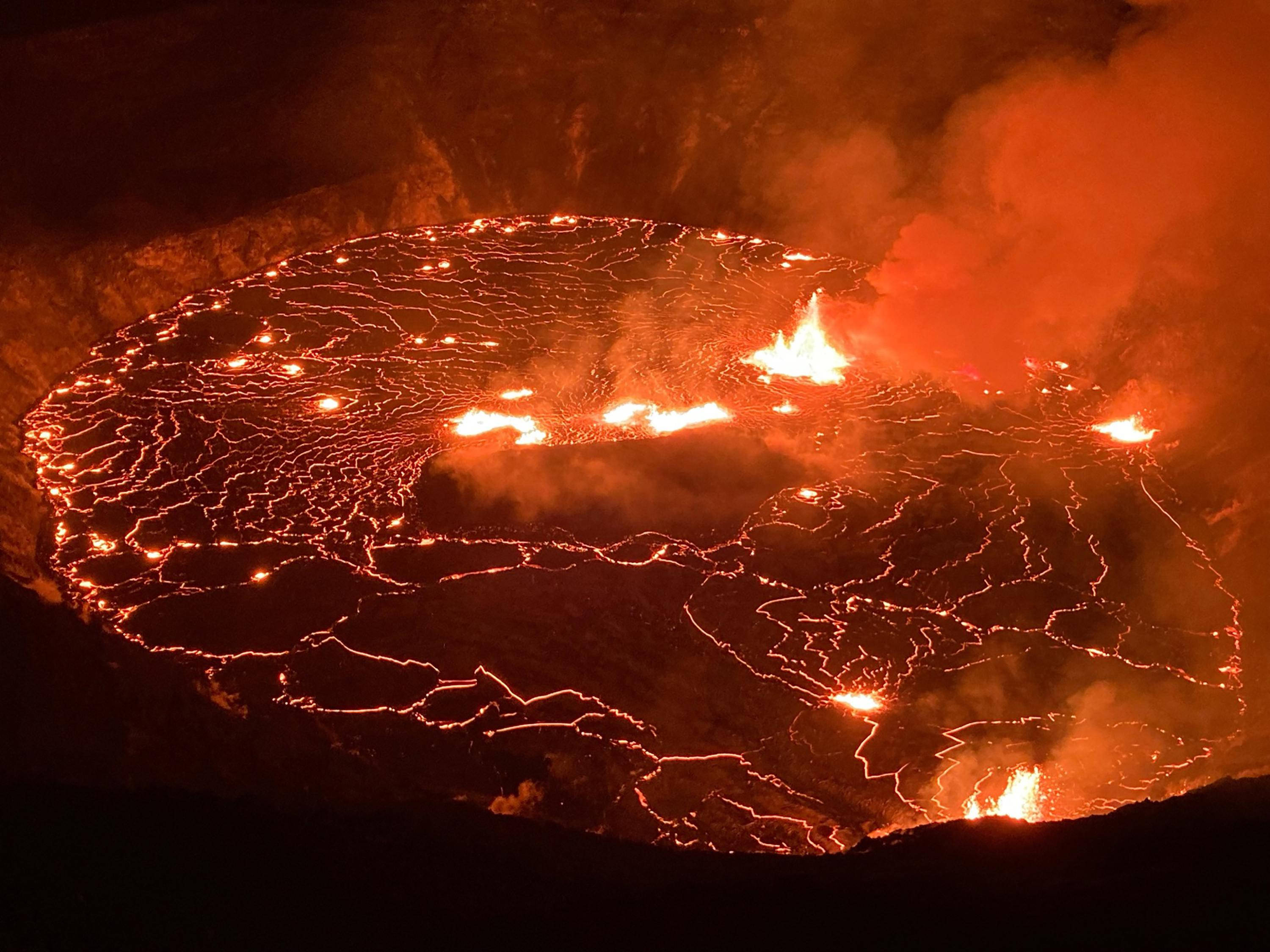 Volcano 桌布 壁紙 — 夜晚的火山口發出光芒，熔岩在其黑暗表面流動，形成複雜的發光圖案。