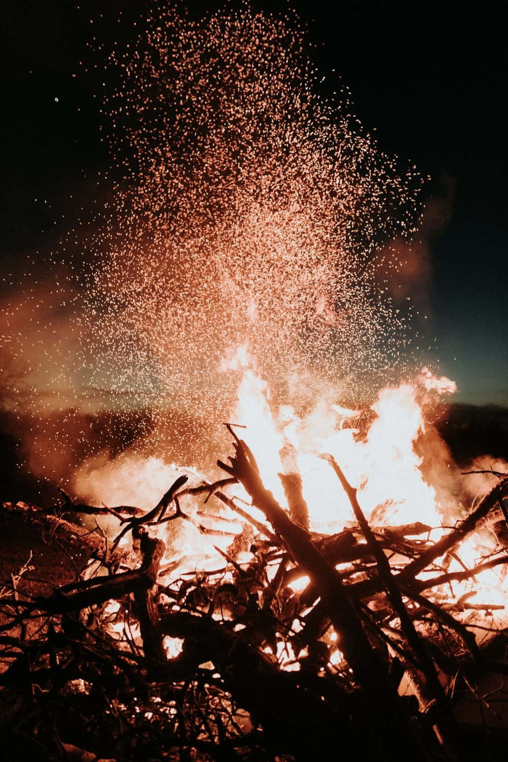 火焰動畫 桌布 壁紙 — 夜晚的營火熊熊燃燒，將發光的餘燼和火花送向黑暗的天空。