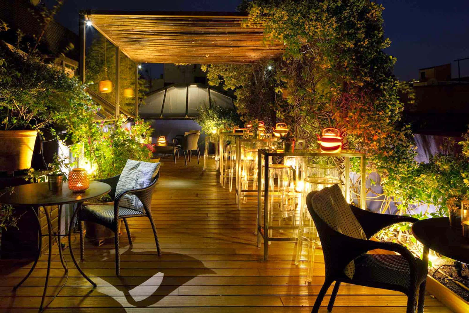 Barcelona 桌布 壁紙 — 夜晚的舒適屋頂露台，溫暖的燈籠和串燈照亮，周圍有茂密的綠植和木質甲板。