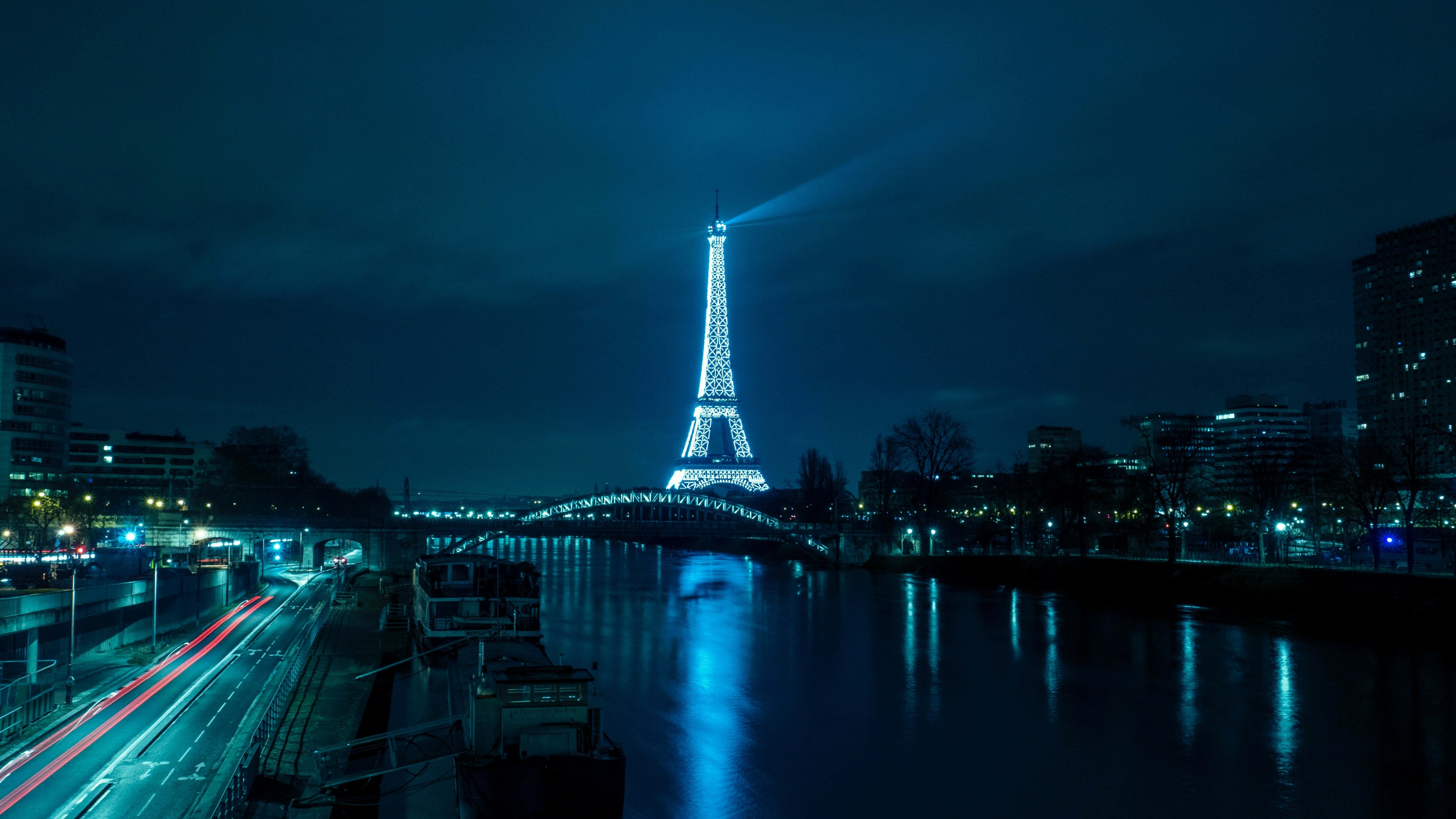Eiffel Tower 桌布 壁紙 — 夜晚的艾菲爾鐵塔被藍色燈光照亮，在塞納河上投射出倒影，並有城市車流的燈光軌跡。