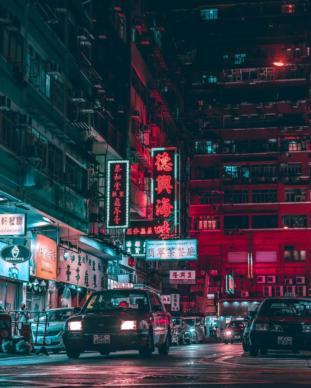  壁紙 — 夜晚的霓虹燈城市街道，高聳的建築物、發光的紅色和藍色招牌，以及濕漉漉的路面上反射出鮮豔燈光的計程車。
