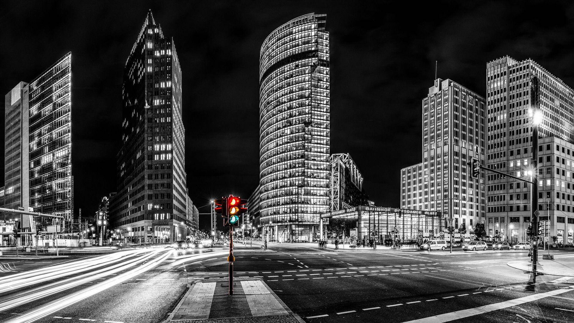 Berlin 桌布 壁紙 — 夜晚的黑白城市景觀，一盞紅色交通燈在汽車燈光拖影和高聳摩天大樓之間閃耀。