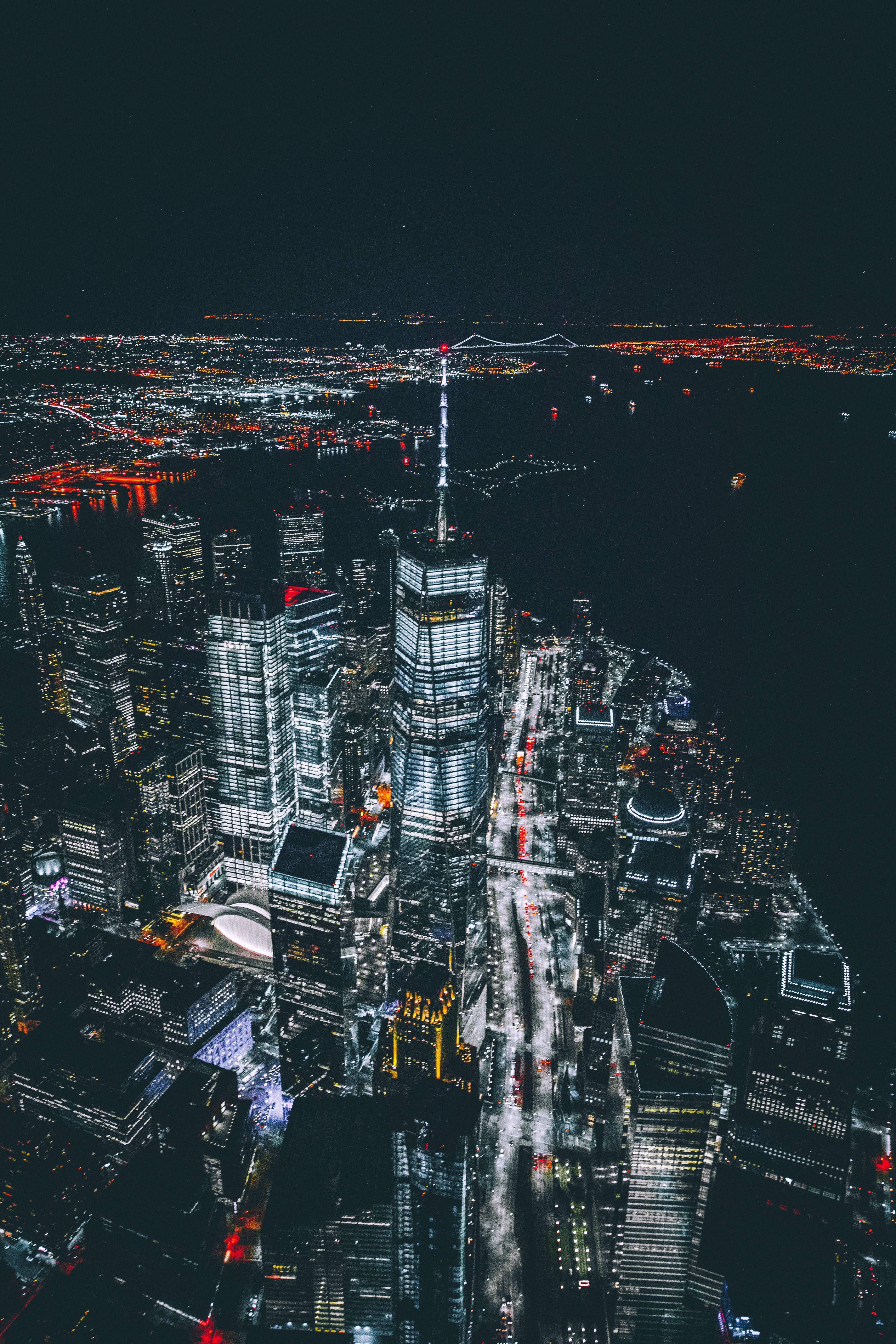 New York 桌布 壁紙 — 夜晚空中俯瞰發光的城市景觀，高聳的摩天大樓和燈火通明的街道倒映在水面上。