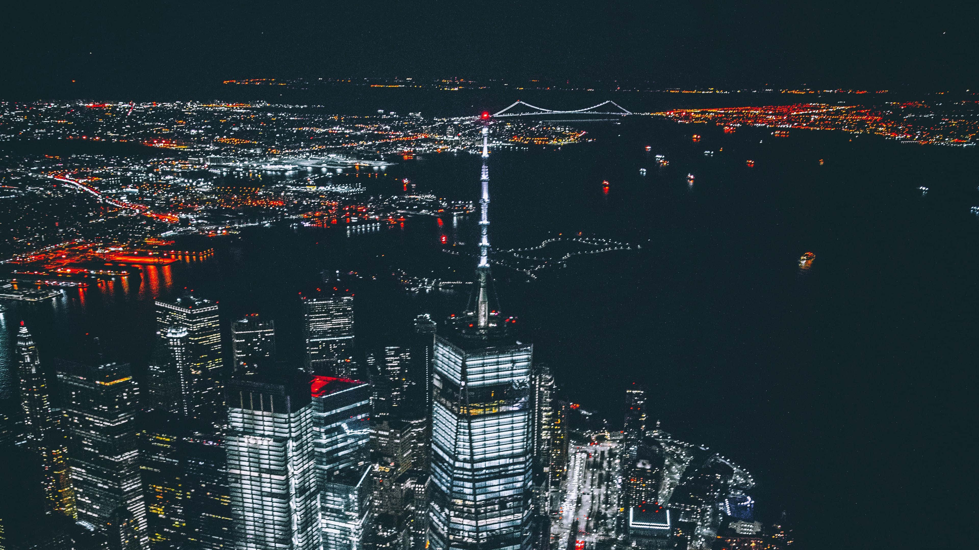 Skyscraper 桌布 壁紙 — 夜晚空中俯瞰閃爍的城市景觀，燈火通明的摩天大樓和橫跨黑暗水面的發光橋樑。