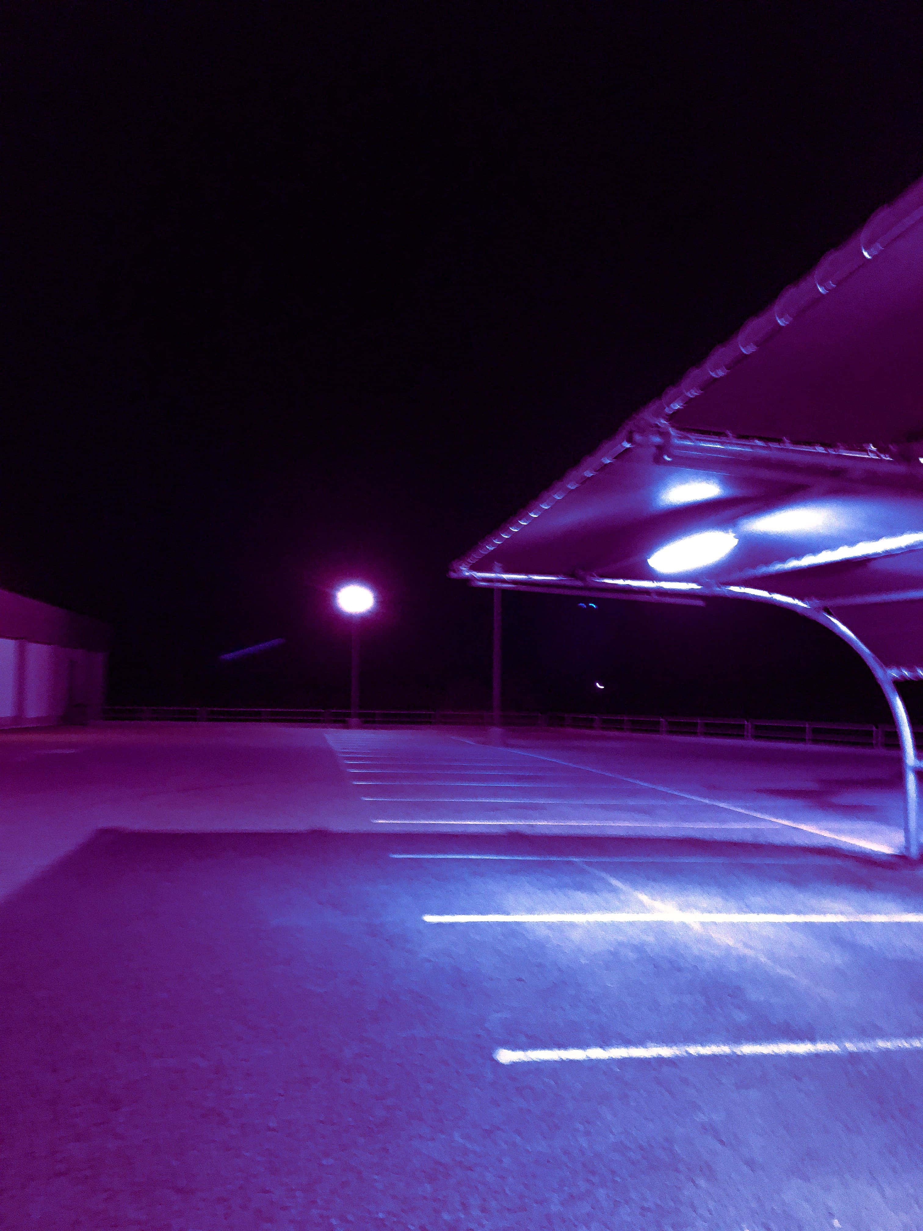 Street 桌布 壁紙 — 夜晚空無一人的停車場，被頭頂燈具和遠處路燈發出的詭異紫色和藍色光芒籠罩。