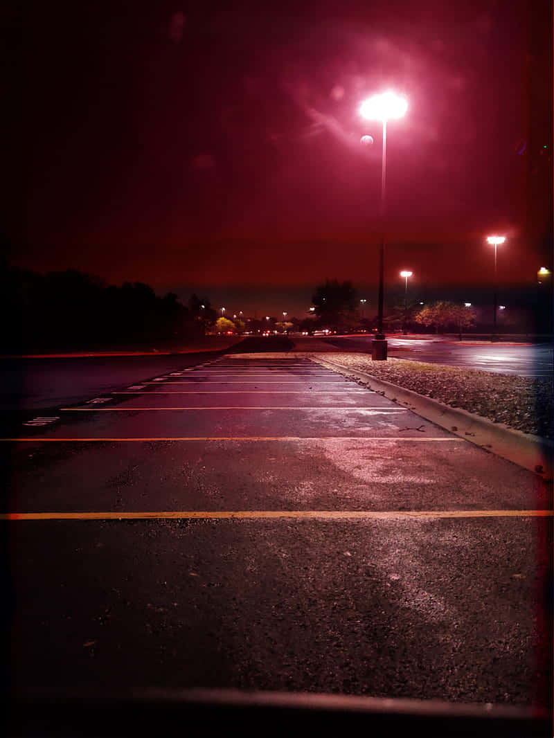 empty 桌布 壁紙 — 夜晚空無一人的停車場，被頭頂街燈發出的詭異紅光籠罩，反射在濕漉漉的瀝青路面上。