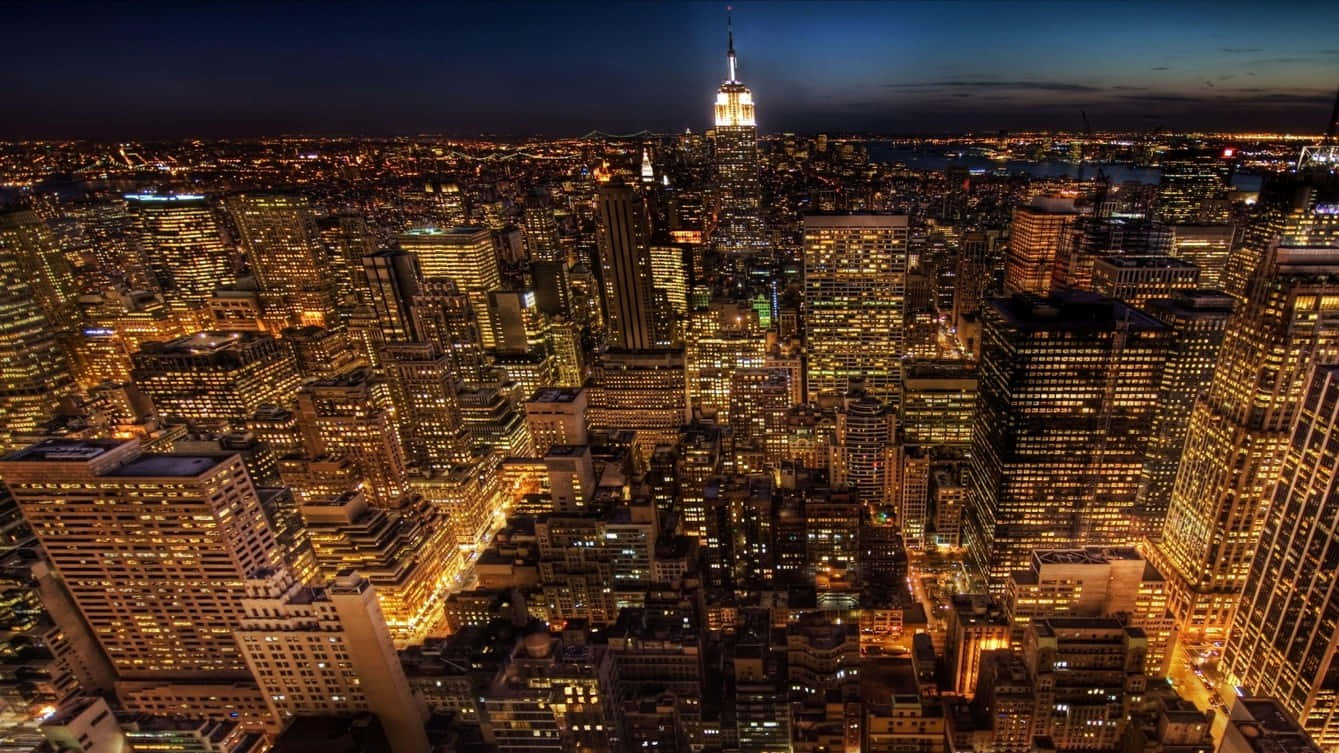 1366x768 Empire State Building 桌布 壁紙 — 夜晚紐約市的空中景觀，摩天大樓閃閃發光，帝國大廈在黑暗的天空中亮起。