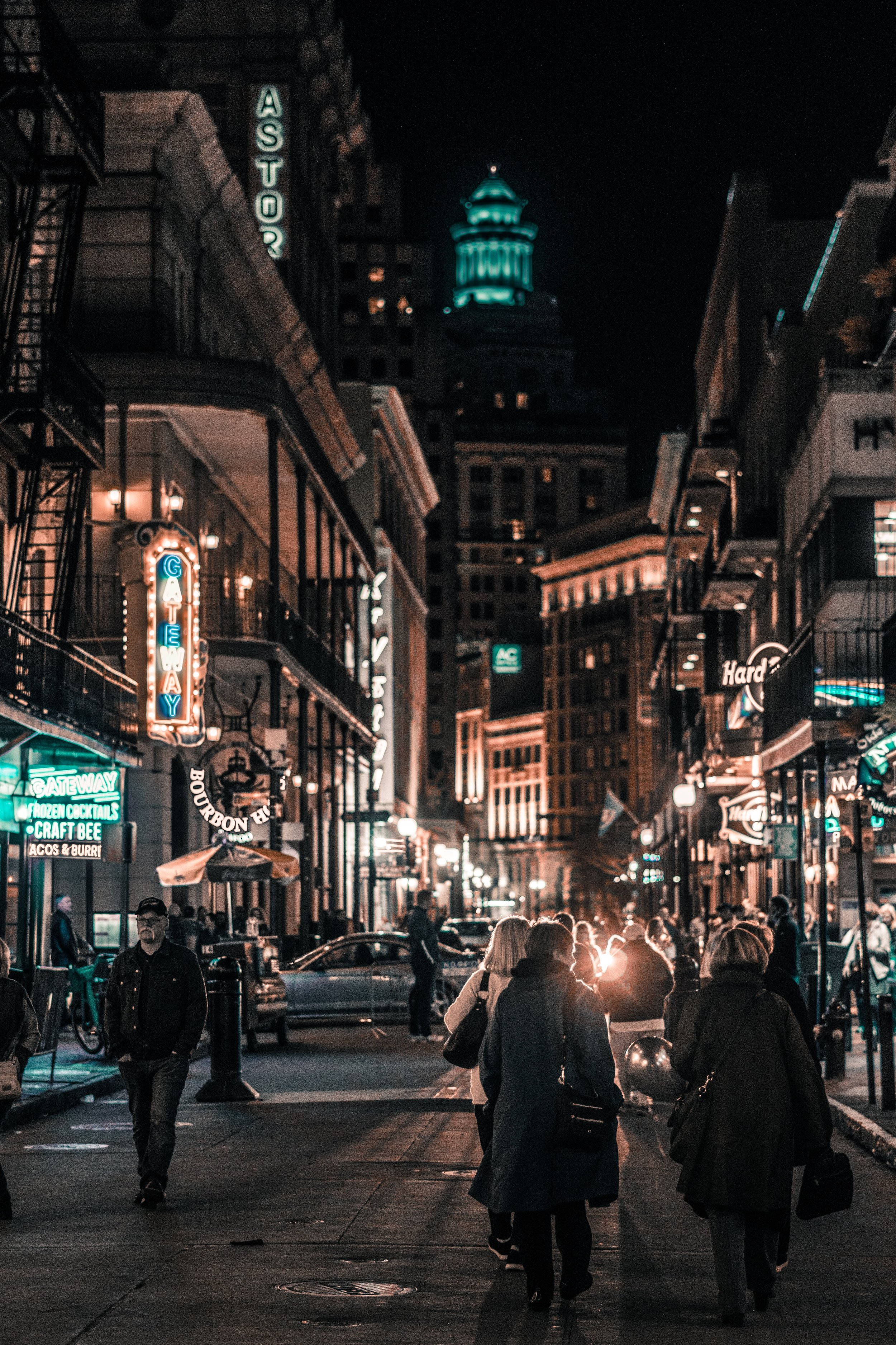 手機 桌布 壁紙 — 夜晚繁忙的城市街道，被閃爍的霓虹燈招牌和溫暖的路燈照亮，行人沿著人行道行走。