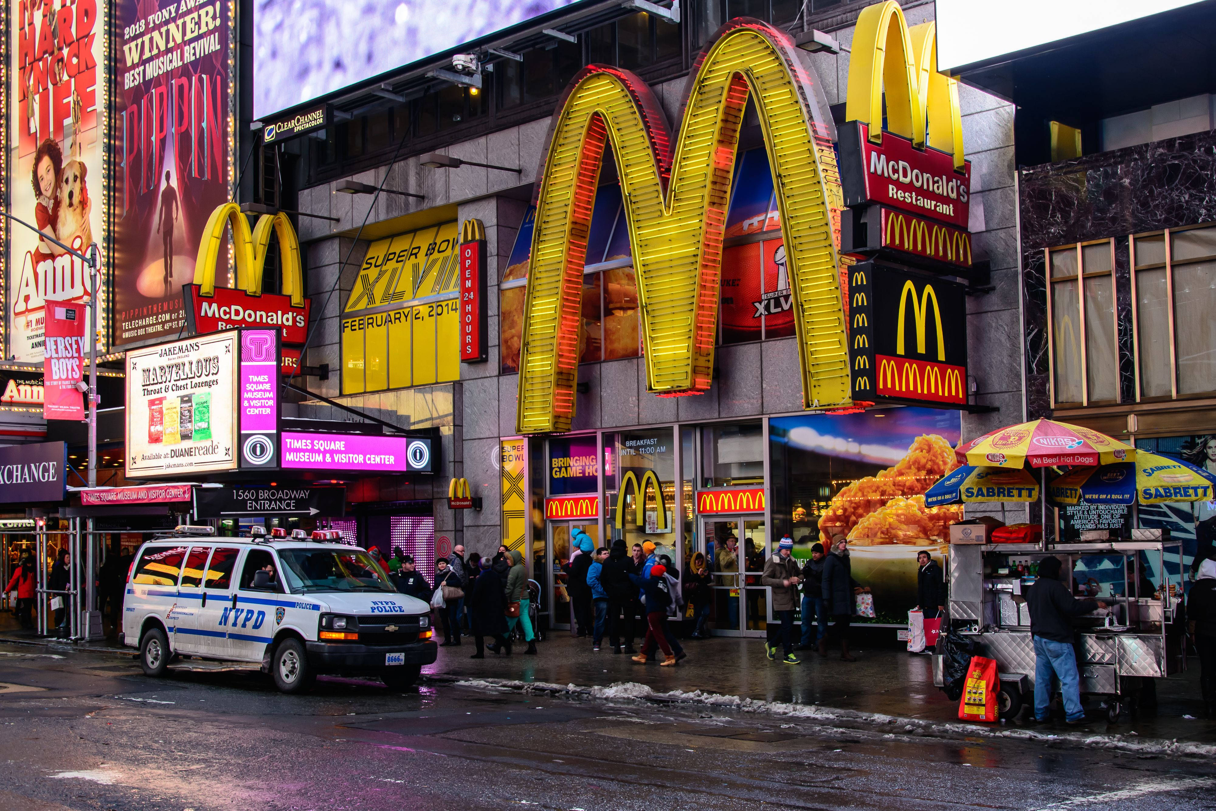 Mcdonalds 桌布 壁紙 — 夜晚繁忙的時代廣場，閃亮的麥當勞、NYPD 廂型車和人群在明亮的廣告牌下。