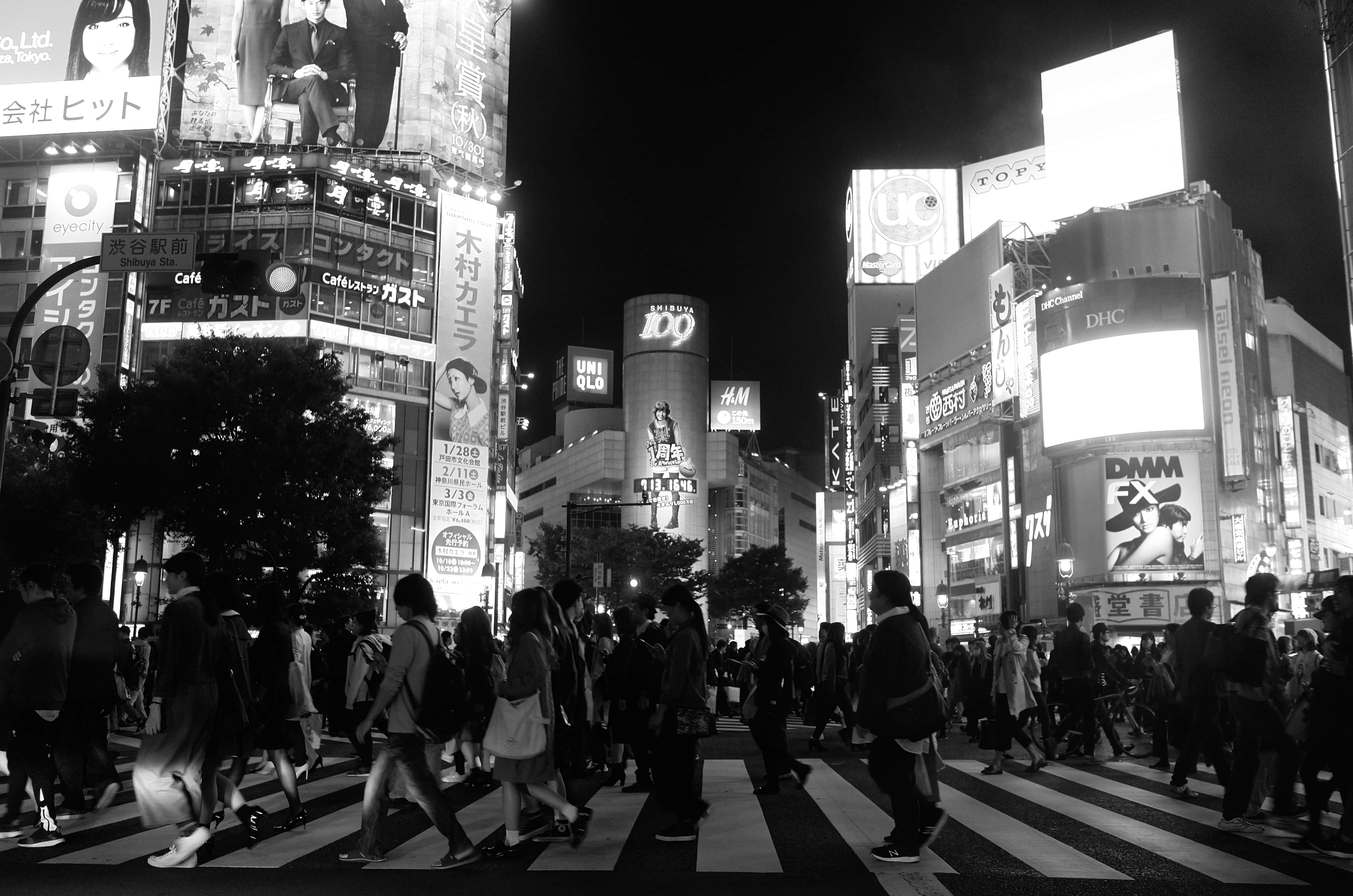日本黑白 桌布 壁紙 — 夜晚繁忙的東京街道，人群在發光的霓虹燈牌和高聳的廣告牌下穿越斑馬線。