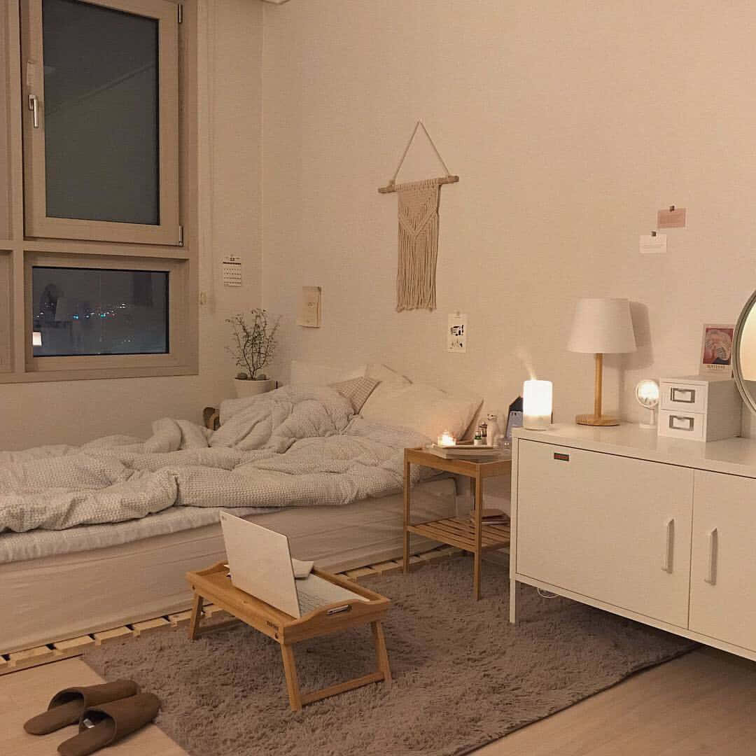 美學米色 桌布 壁紙 — 夜晚舒適的臥室，配有柔和燈光、一張床、木架上的筆記型電腦，以及透過窗戶看到的城市燈光景色。