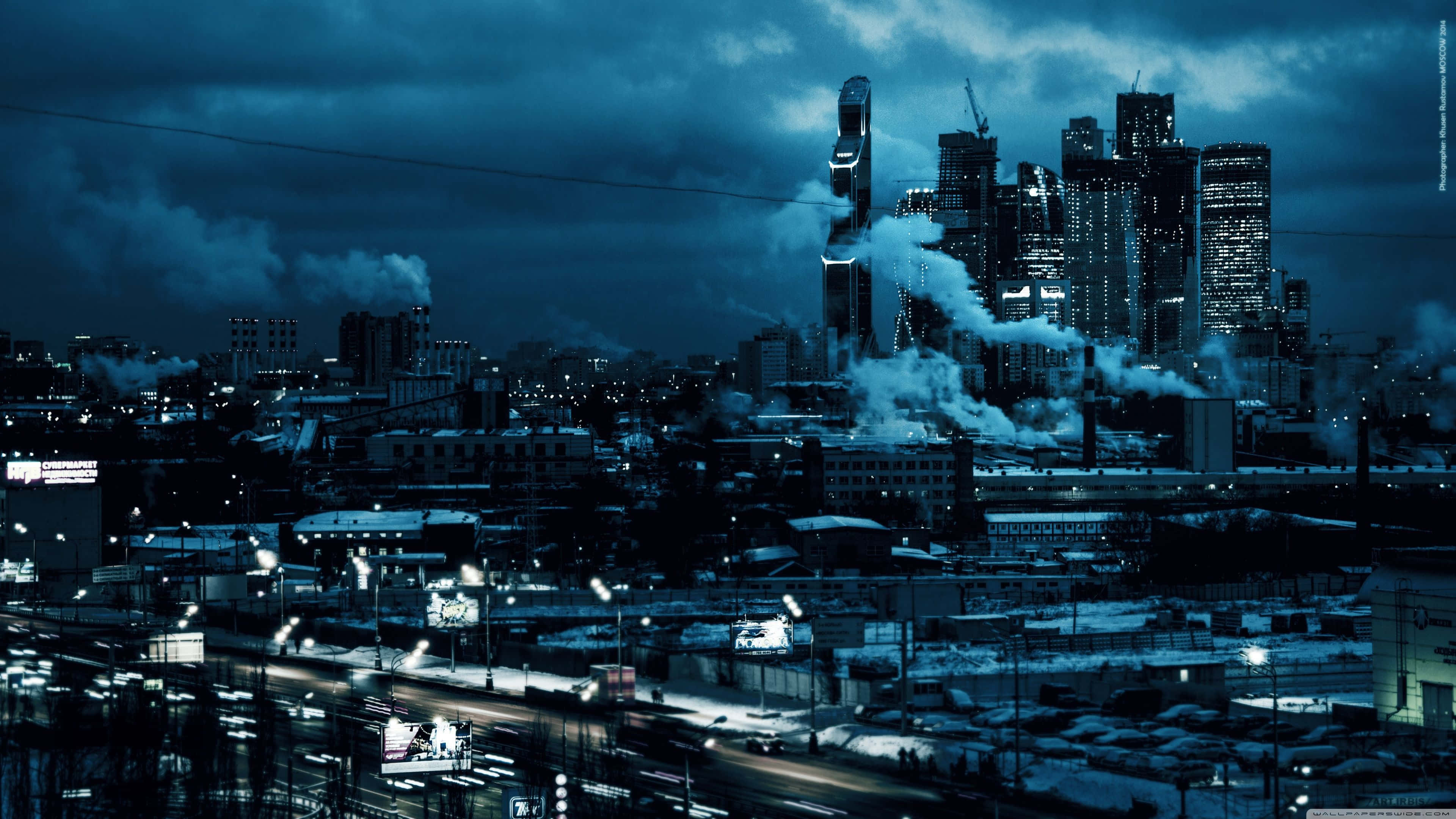 Industrious 桌布 壁紙 — 夜晚藍色調的憂鬱城市景觀，工業建築升起的煙霧和發光的燈光照亮積雪的街道。