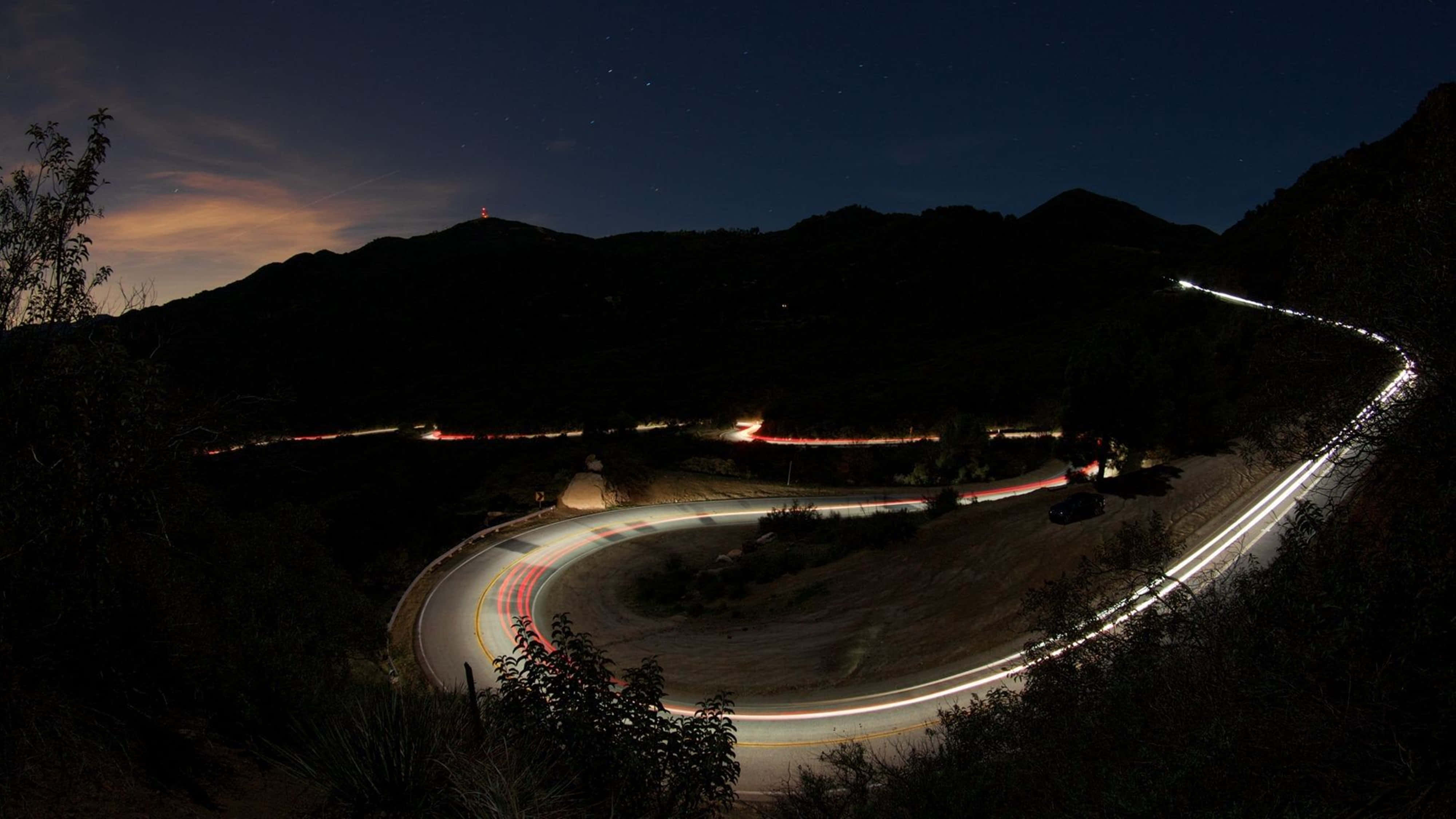 桌布 壁紙 — 夜晚蜿蜒的山路，在星空下被汽車燈光軌跡照亮。