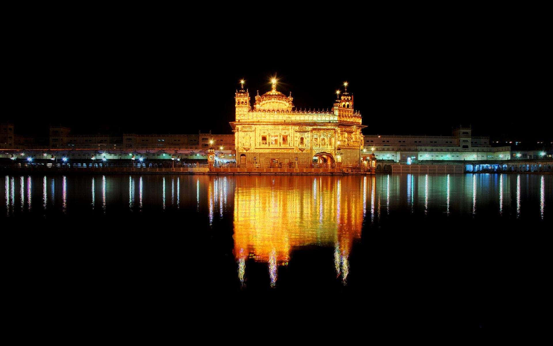 Golden Temple 桌布 壁紙 — 夜晚被照亮的金色寺廟在黑暗天空下的平靜水面上燦爛地倒映。