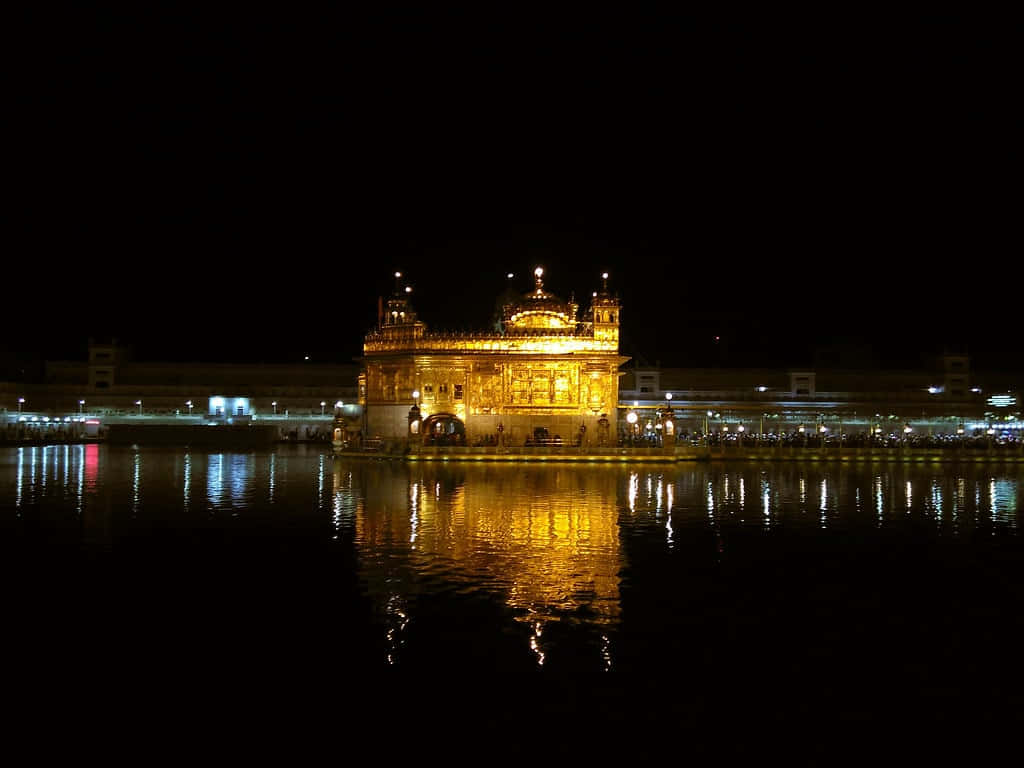 Golden Temple 桌布 壁紙 — 夜晚被照亮的金色寺廟在黑暗的天空下溫暖地倒映在平靜的水面上。
