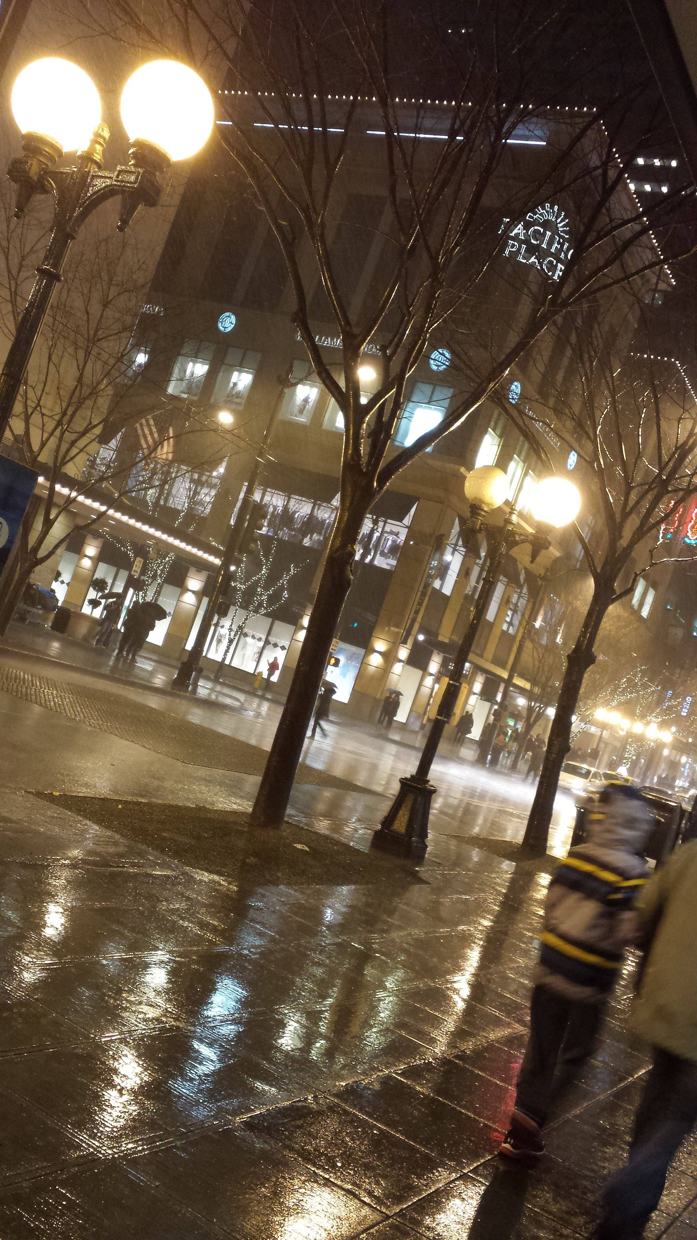 Rainy Day 桌布 壁紙 — 夜晚被雨水浸濕的城市人行道，發光的街燈和光禿禿的樹木倒映在濕漉漉的路面上。