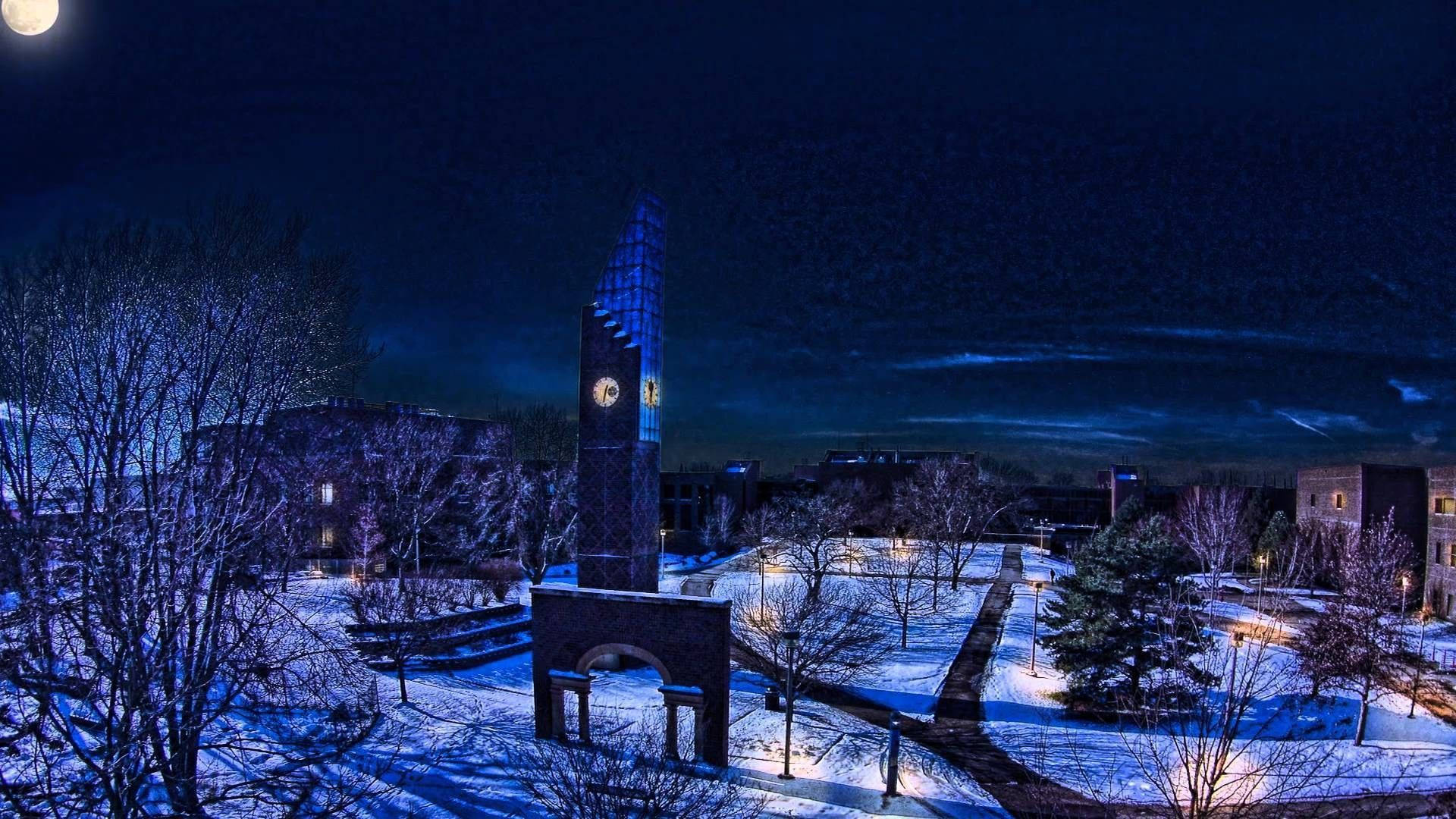 Minnesota 桌布 壁紙 — 夜晚被雪覆蓋的校園，在滿月和深藍色天空下有一座發光的鐘樓。
