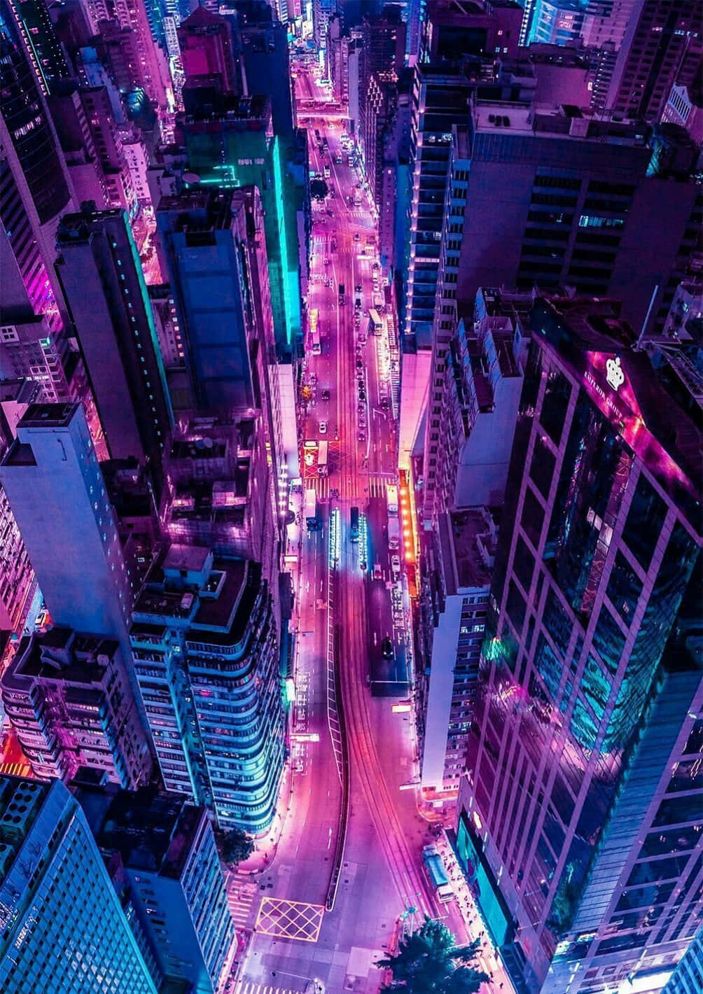 Aesthetic Dark Pink 桌布 壁紙 — 夜晚被霓虹燈淹沒的城市街道鳥瞰圖，高聳的摩天大樓散發著電光紫和青色調。