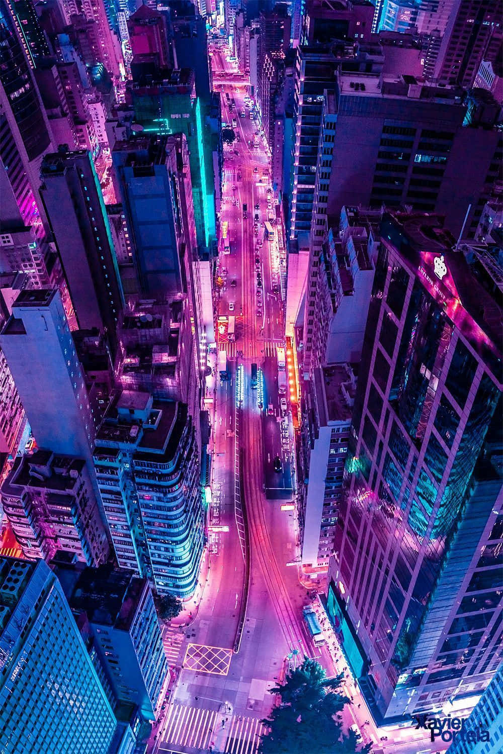 iPhone Neon 桌布 壁紙 — 夜晚被霓虹燈淹沒的城市街道鳥瞰圖，高聳的摩天大樓散發著電光紫和藍色調。