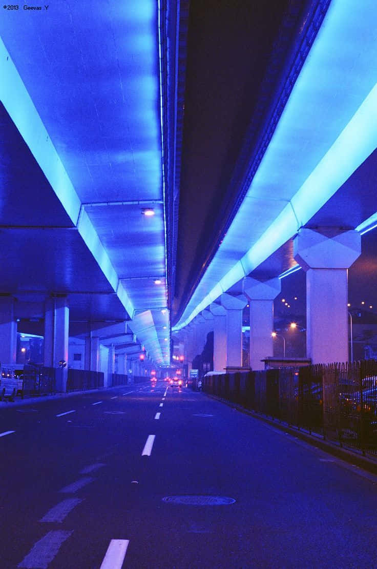 霓虹藍美學 桌布 壁紙 — 夜晚被霓虹藍光照亮的高速公路地下道，匯合的車道和遠處的車燈。