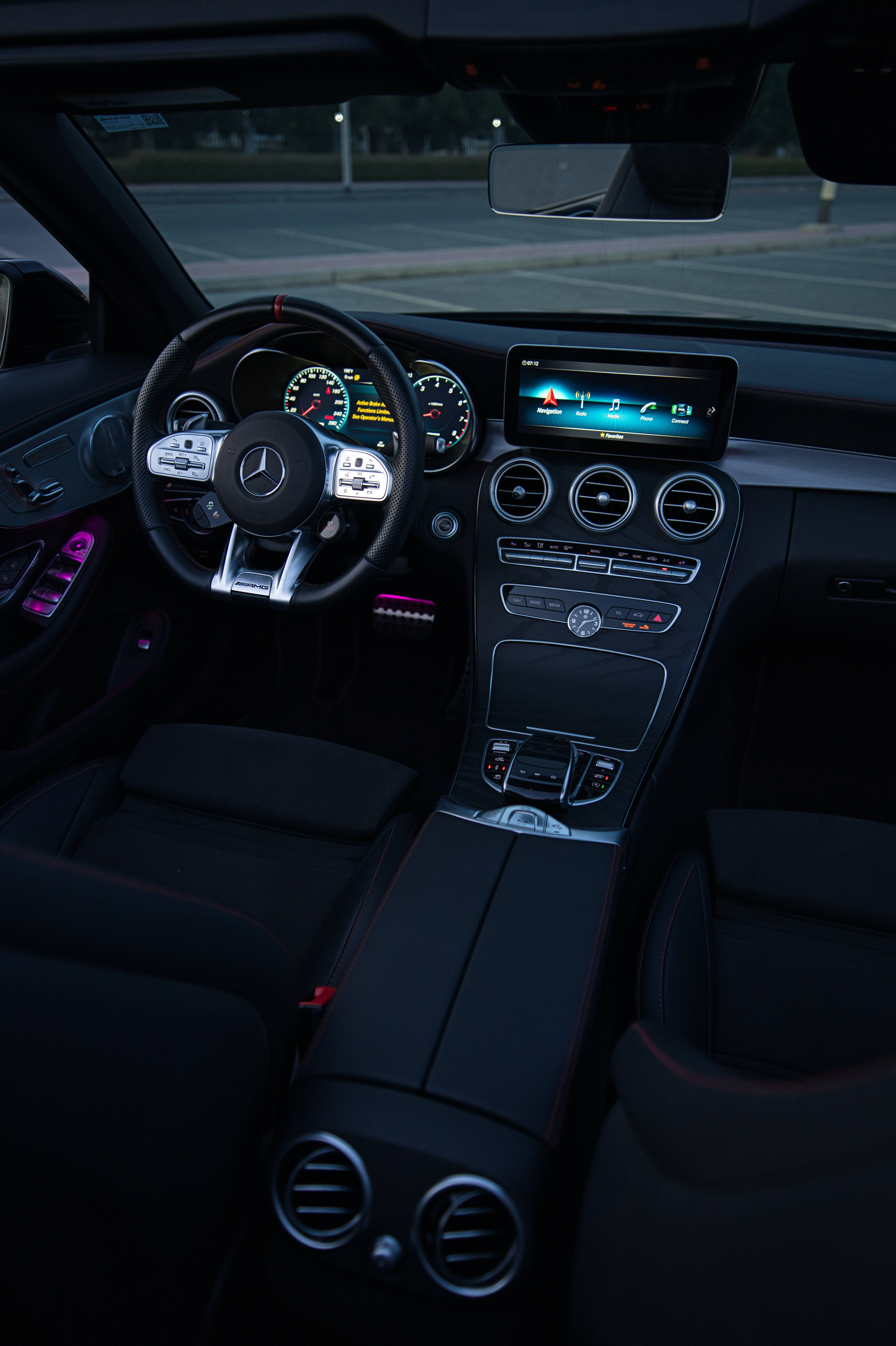 mercedes amg iPhone 桌布 壁紙 — 夜晚豪華車內裝，帶有發光數位儀表板和黑色皮革座椅上的環境紫色燈光。