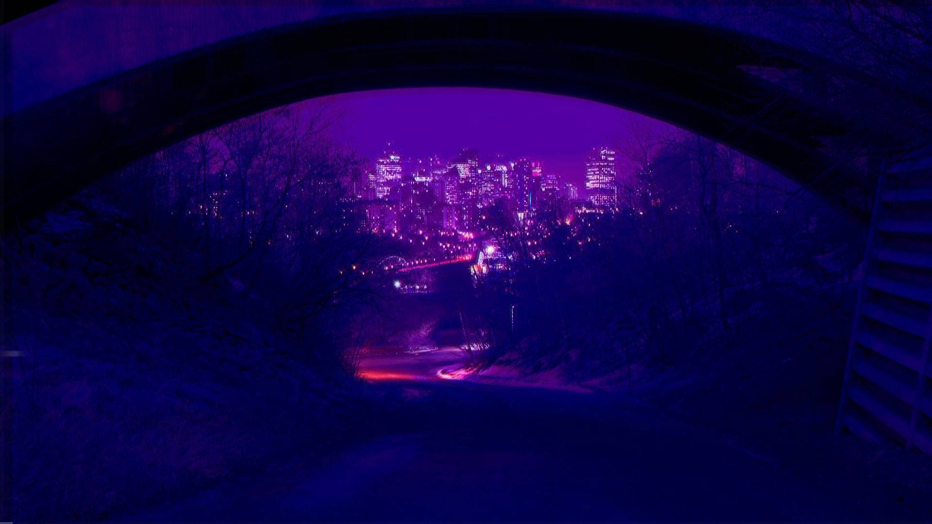 暗紫色美學 桌布 壁紙 — 夜晚透過深色石拱門看到的紫色城市景觀，帶有發光的燈光和光禿禿的樹木。