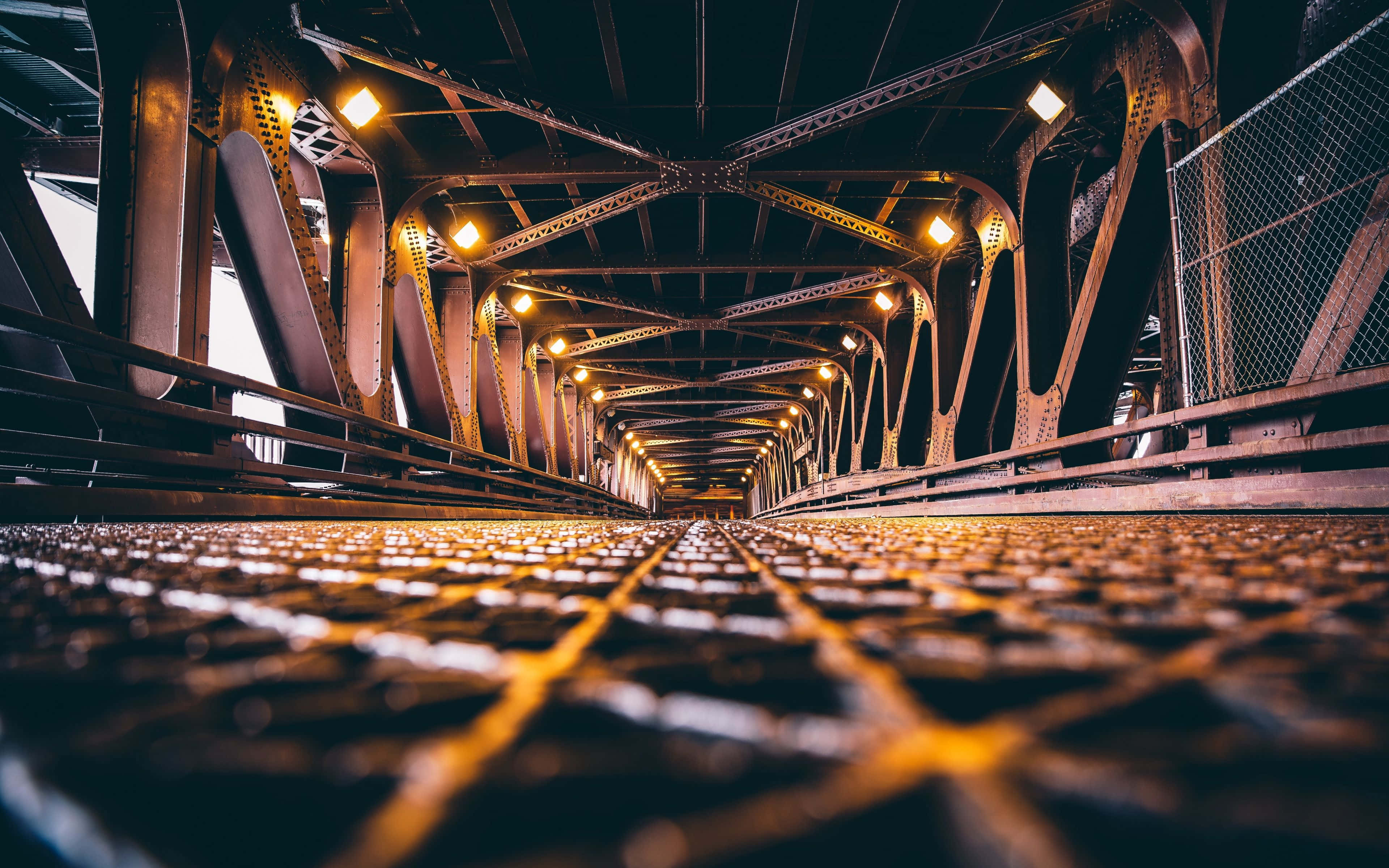 Infrastructure 桌布 壁紙 — 夜晚透過鋼桁架橋的低角度視野，溫暖的發光燈光照射著金屬結構。