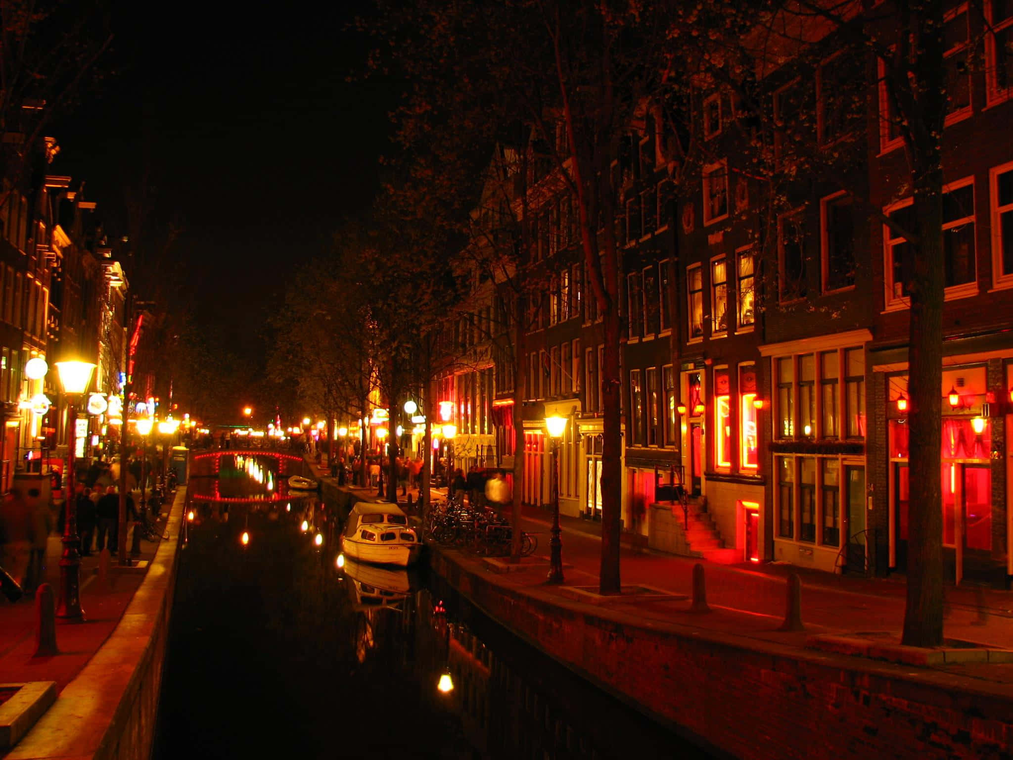 Red Light District 桌布 壁紙 — 夜晚阿姆斯特丹一條狹窄的運河，溫暖的路燈和紅色霓虹燈在黑暗的水面上閃爍倒影。