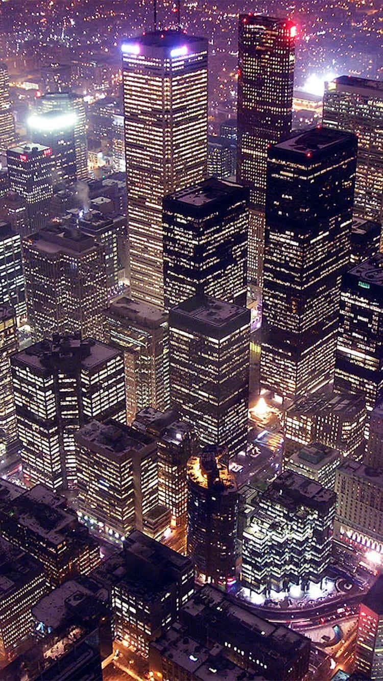 City iPhone 桌布 壁紙 — 夜晚雪景城市天際線的鳥瞰圖，高聳的摩天大樓在黑暗的天空中閃爍著溫暖的燈光。