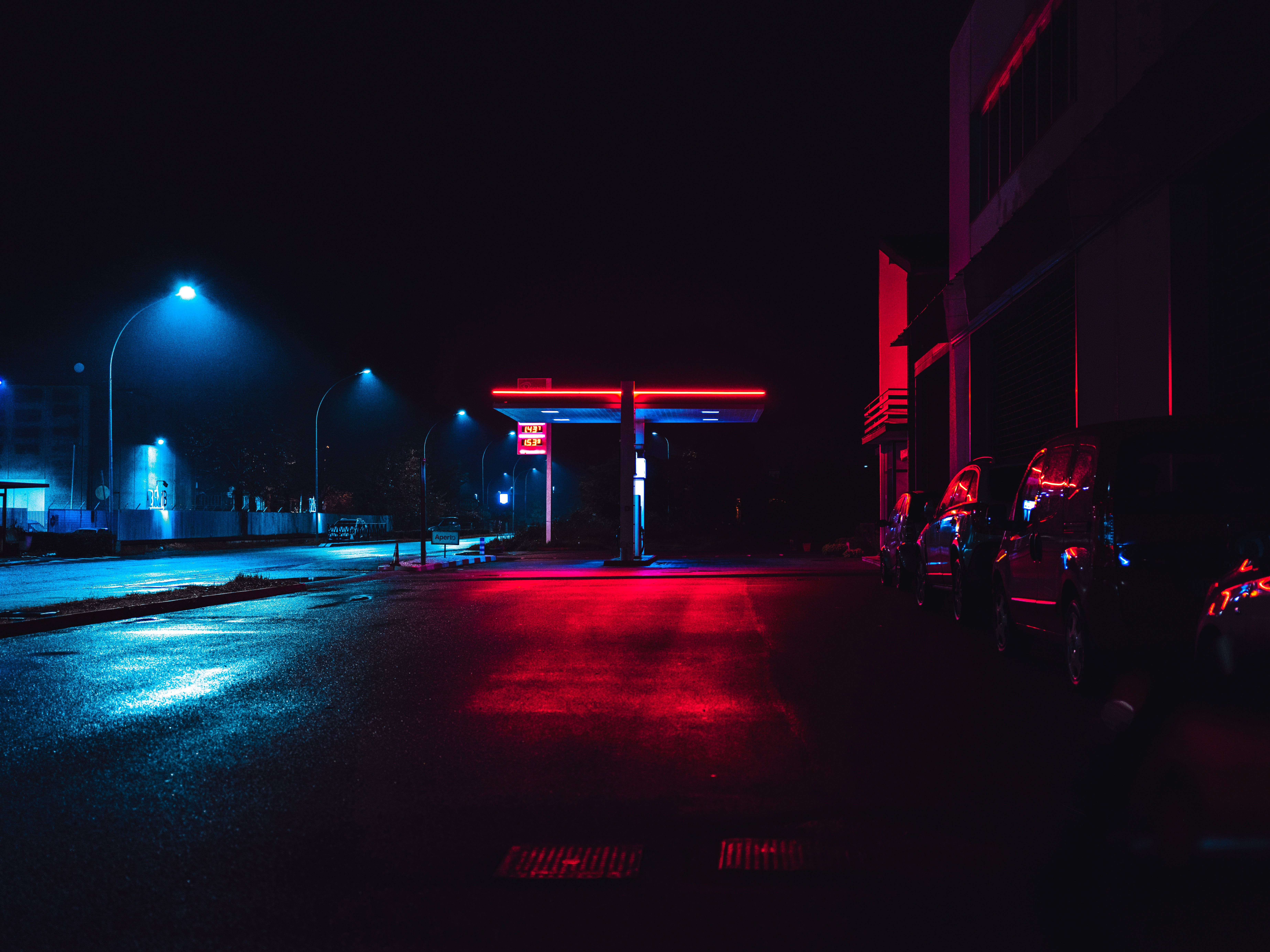 霓虹城市動態圖 桌布 壁紙 — 夜晚霓虹燈加油站，紅色和藍色燈光在黑暗天空下反射在濕漉漉的路面上。
