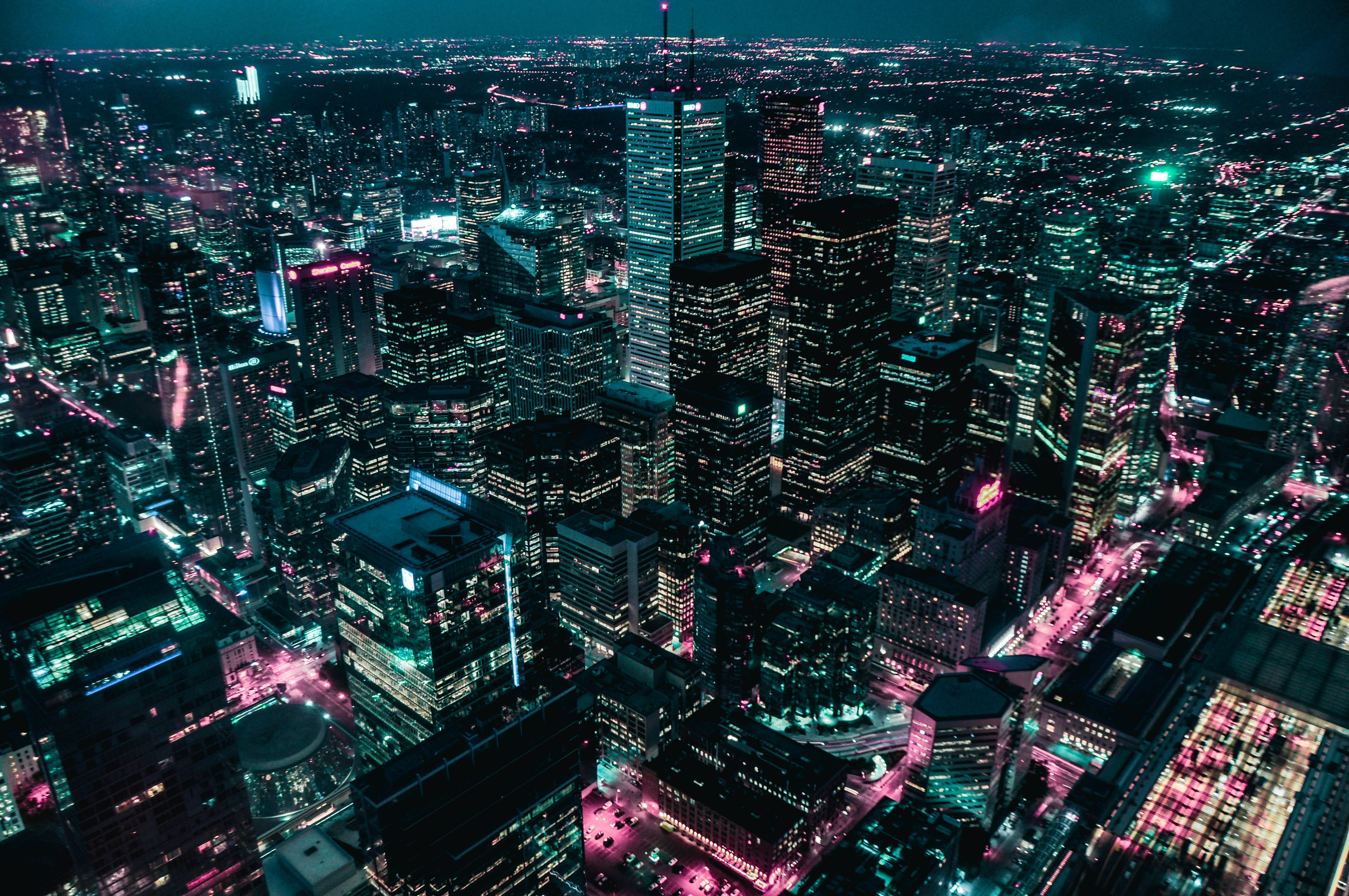 City At Night 桌布 壁紙 — 夜晚霓虹燈照亮城市景觀的鳥瞰圖，高聳的摩天大樓閃爍著青綠色和洋紅色調。