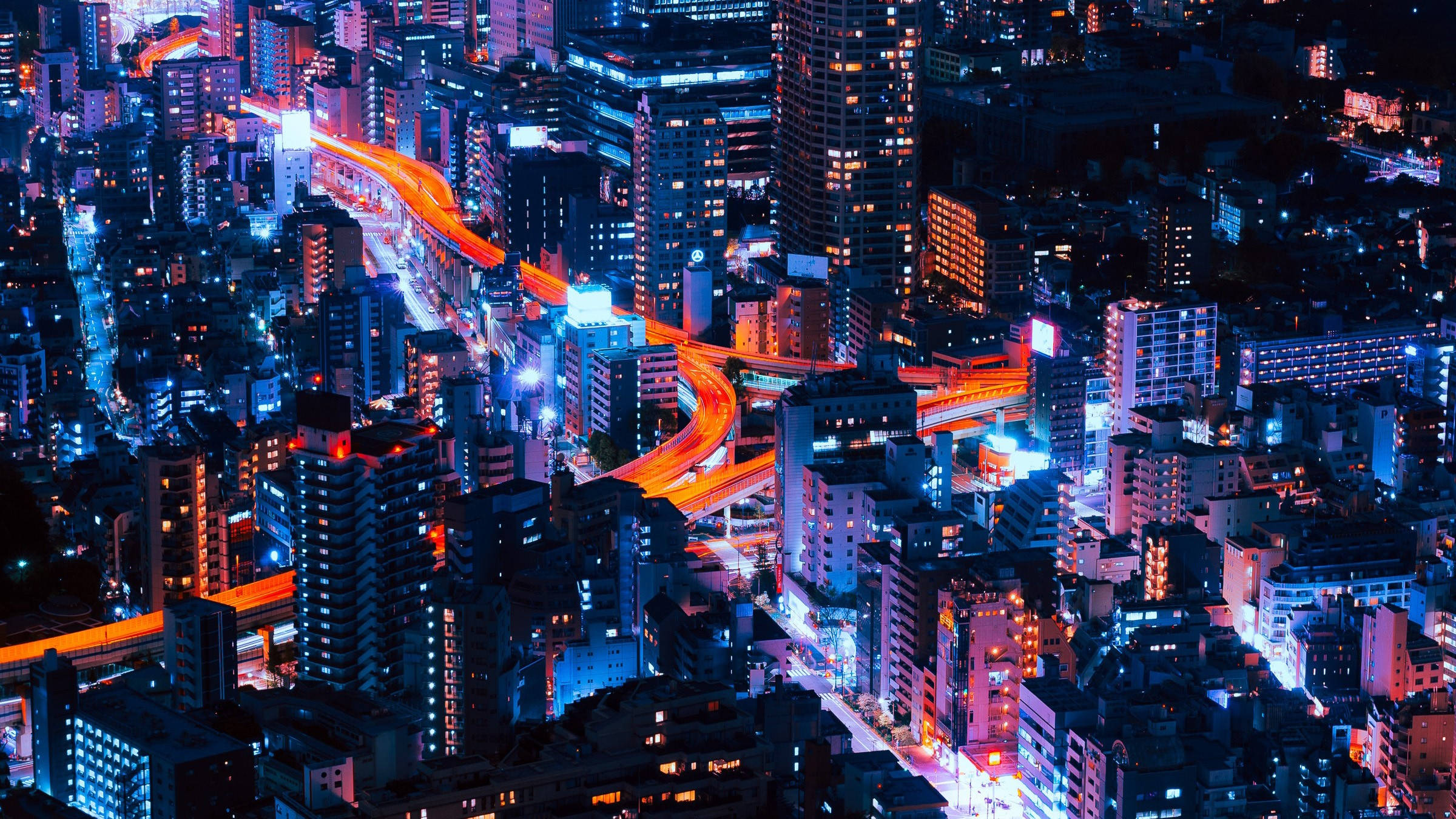 Asia 桌布 壁紙 — 夜晚霓虹燈照亮城市景觀的鳥瞰圖，發光的橙色高速公路蜿蜒穿過高聳的建築物。